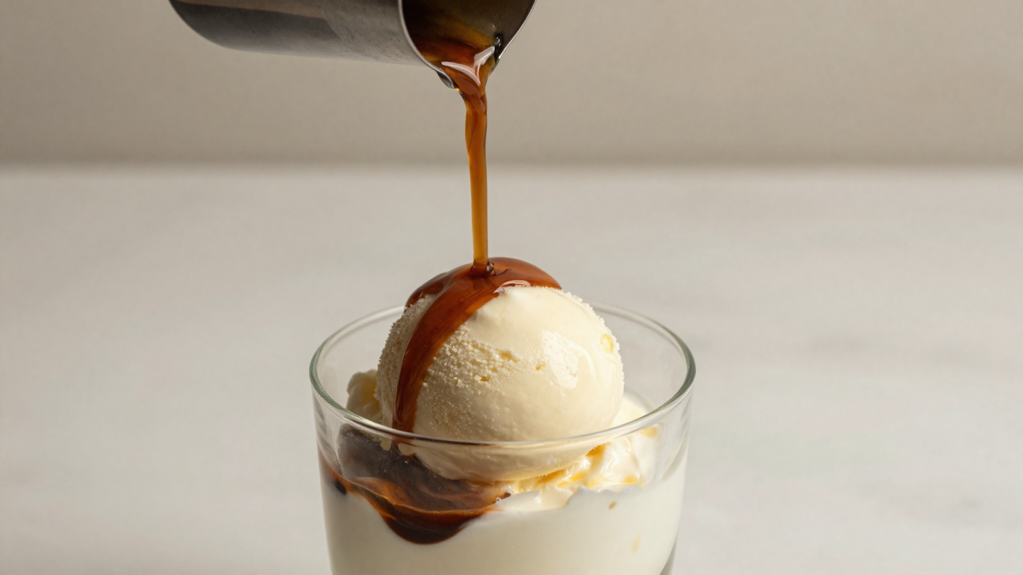 Close-up of a vanilla fior di latte gelato scoop being drowned in fresh espresso in a clear glass