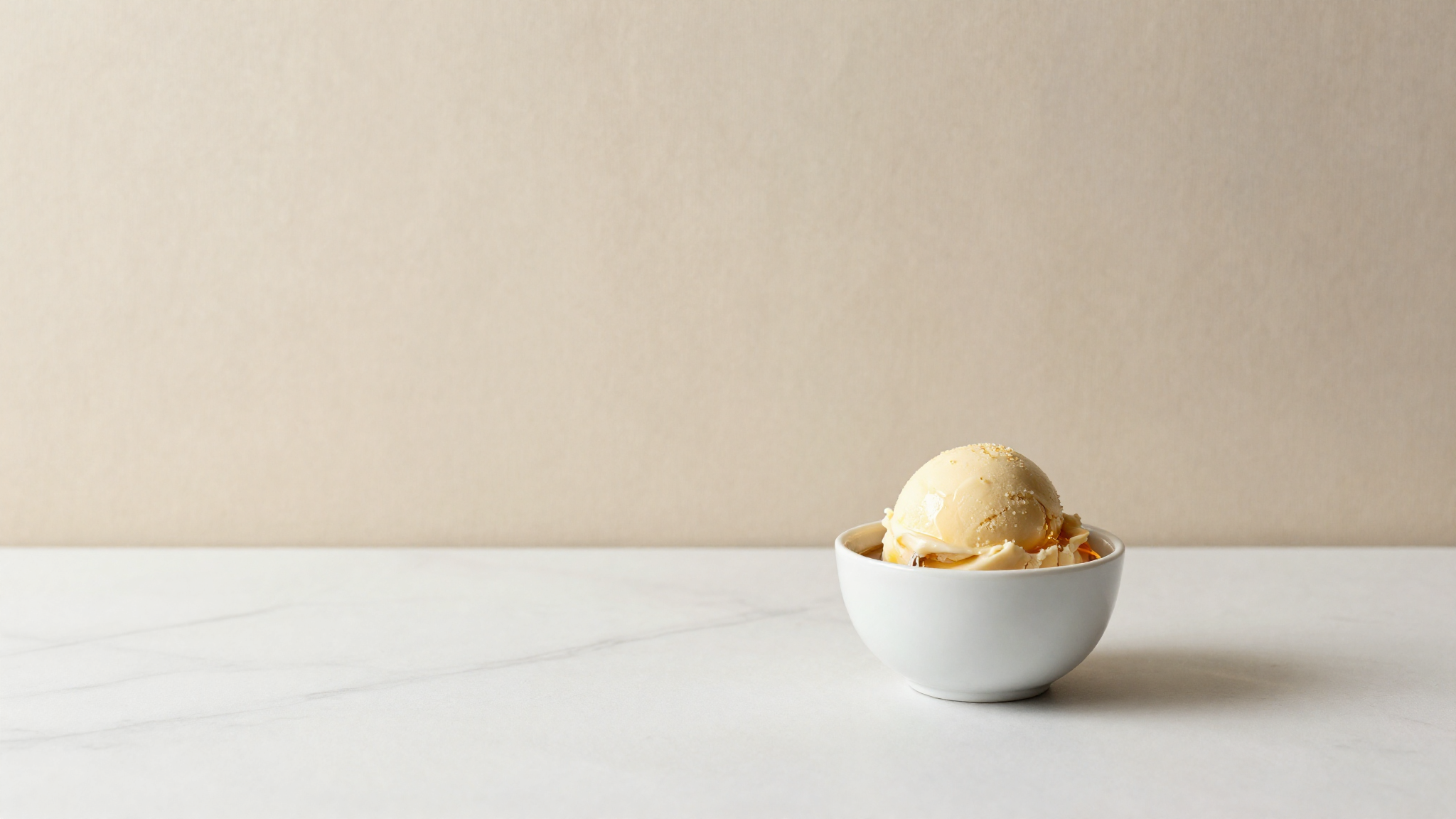 A glass of amber liqueur beside a scoop of gelato on marble evoking freezing balance