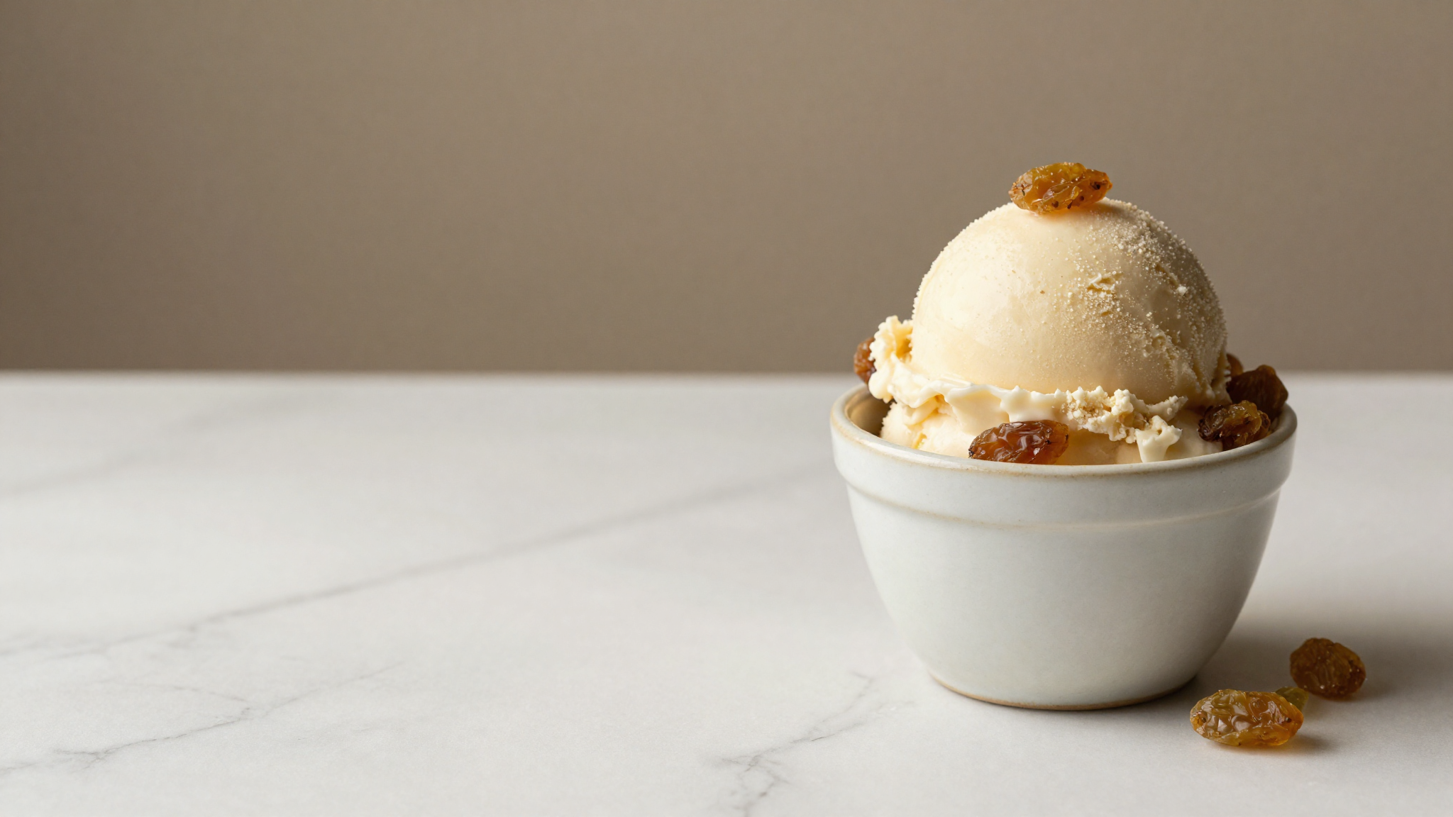 Scoop of finished rum-raisin gelato in a ceramic cup with plump soaked raisins visible