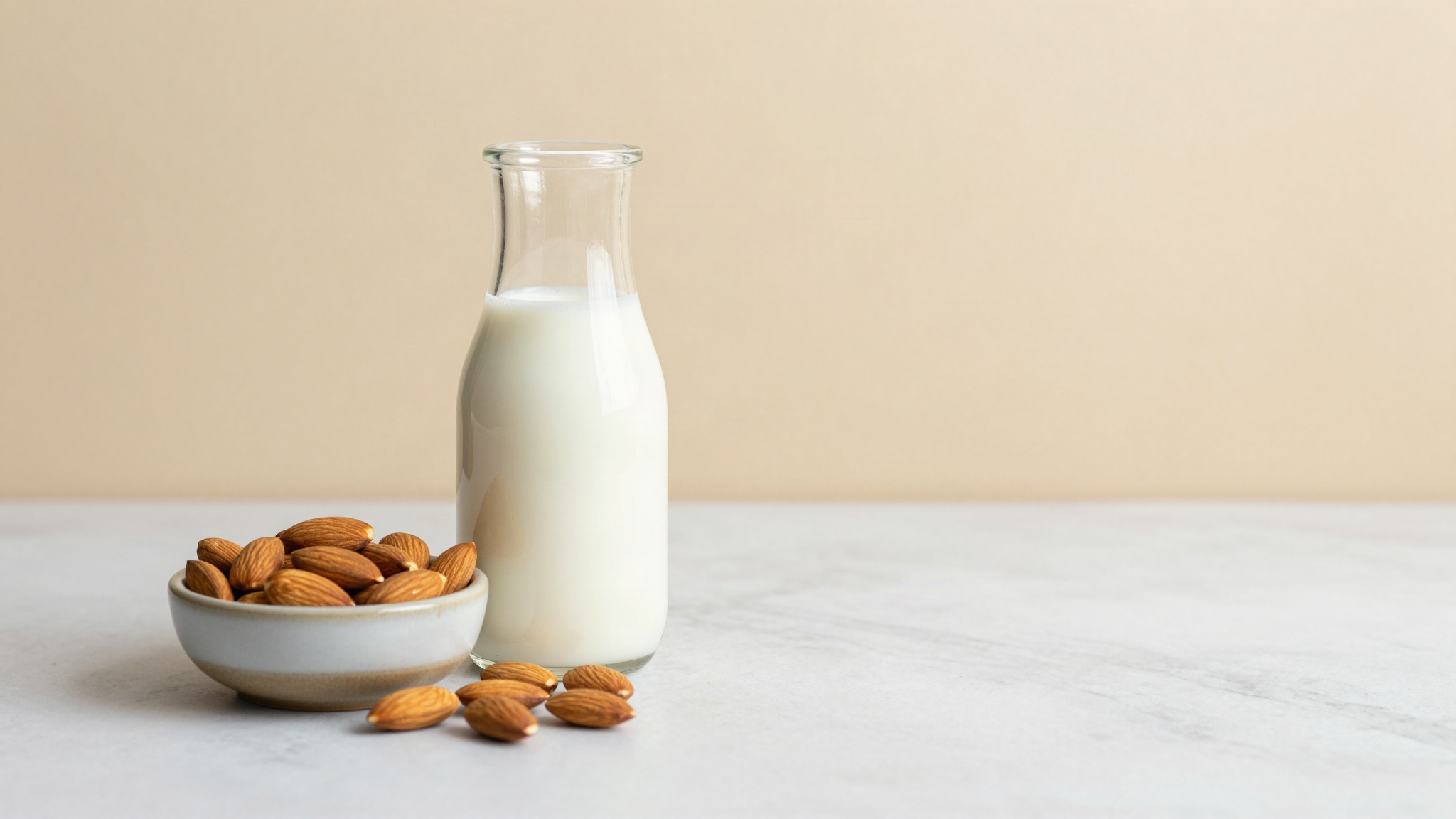Glass carafe of almond milk beside raw whole almonds on a marble surface
