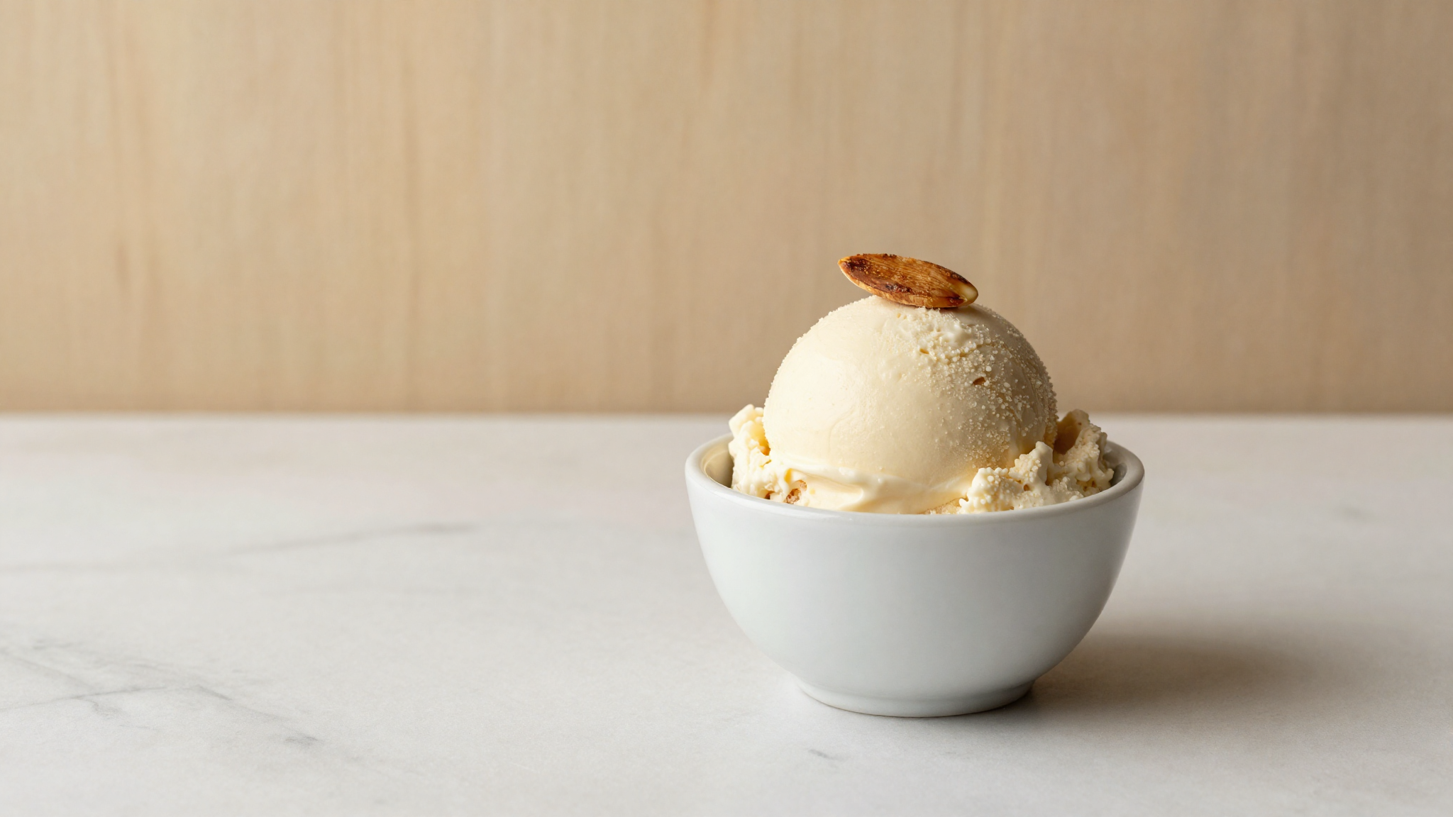 Finished scoop of pale ivory almond gelato in a white ceramic cup, garnished with a sliver of toasted almond