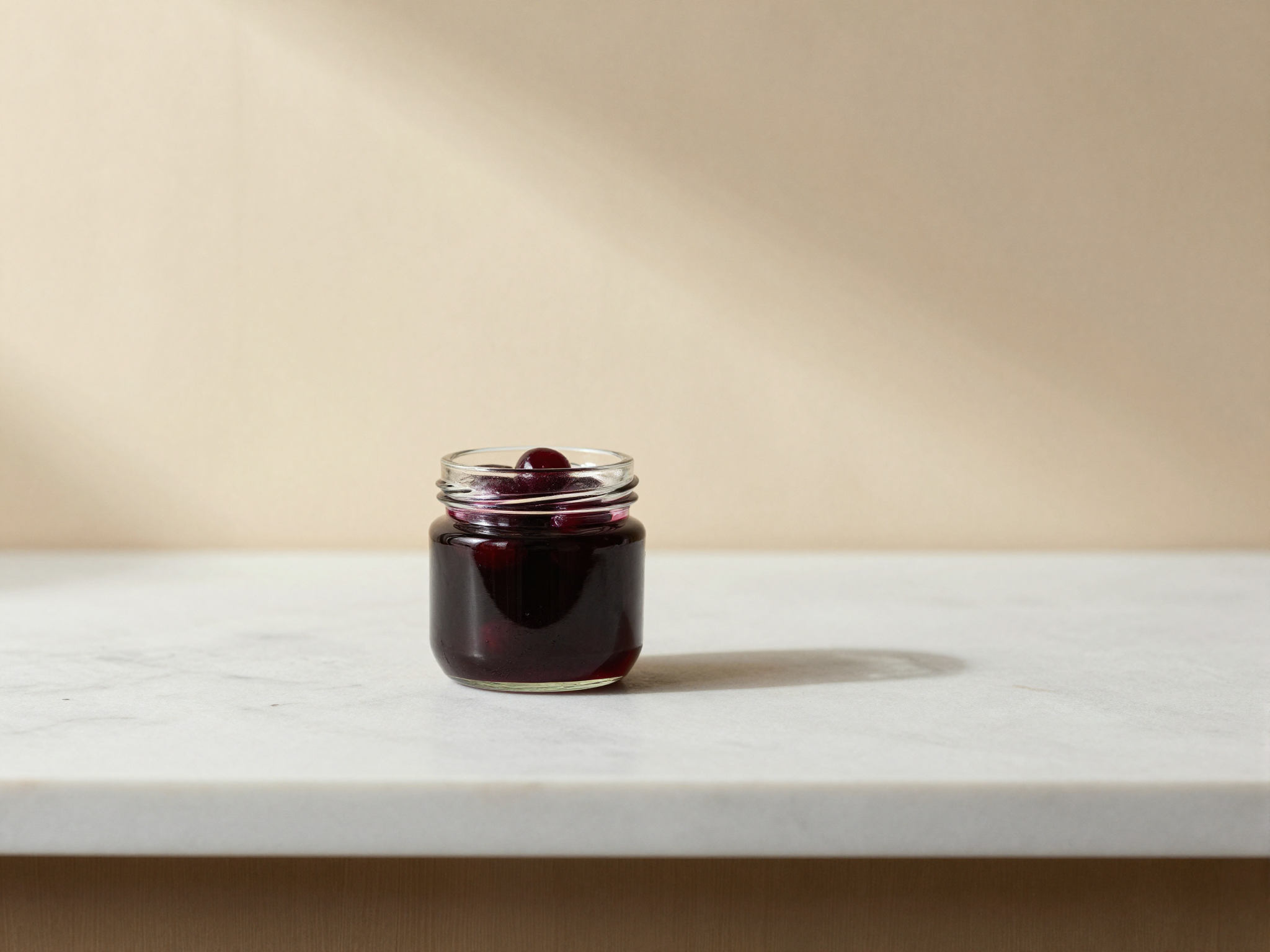 A small glass jar of dark amarena cherries in glossy ruby syrup on a marble counter