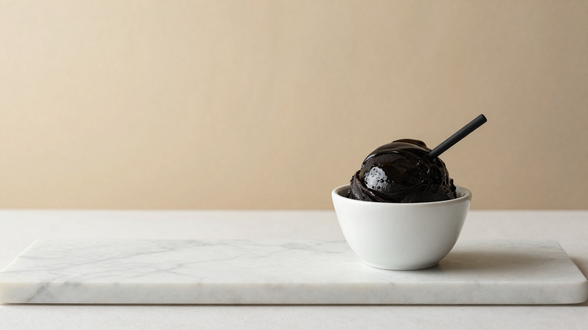 Glossy jet-black Italian licorice gelato in a white ceramic cup garnished with a licorice stick