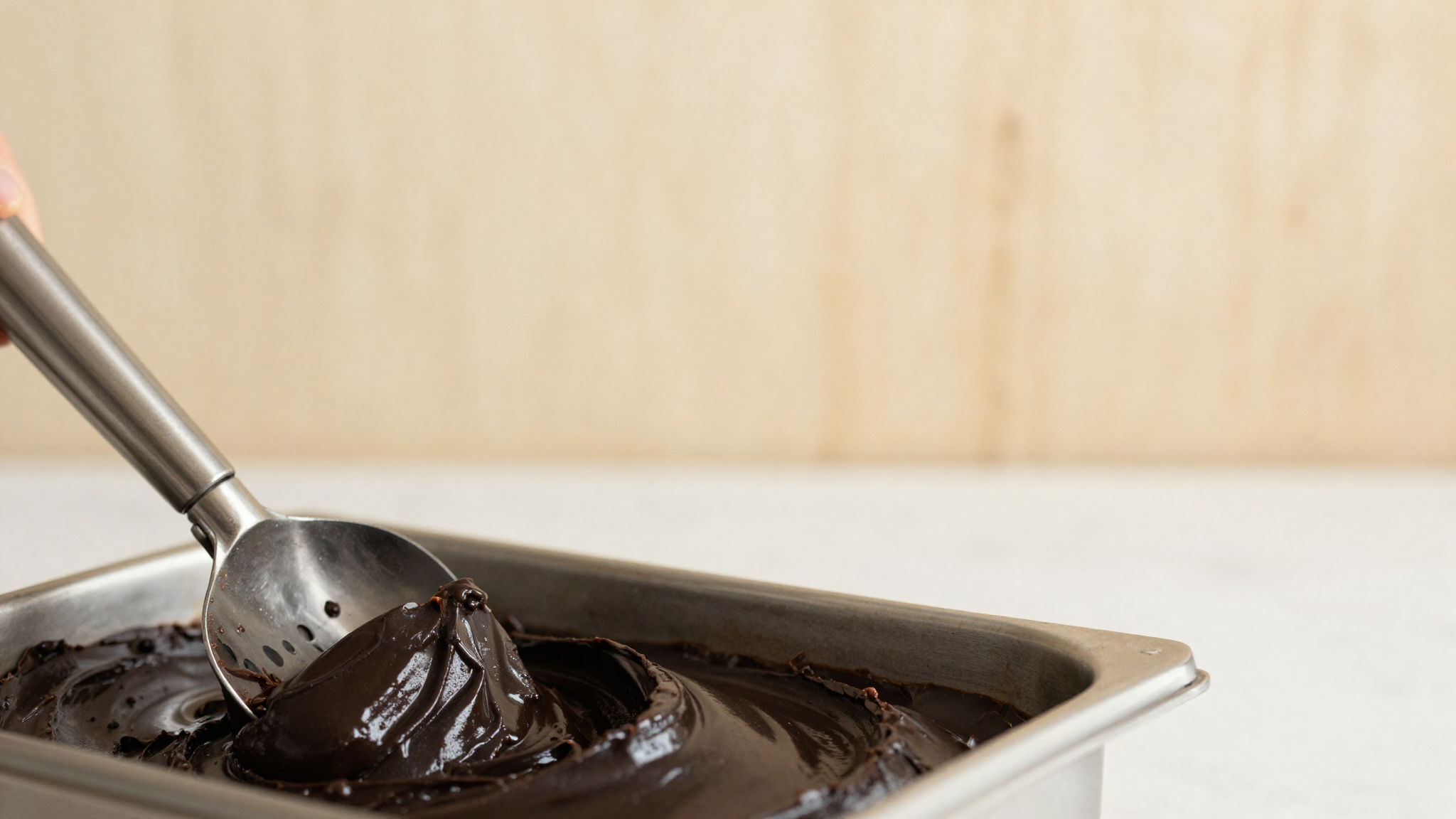 Close-up of a stainless gelato batch-freezer paddle churning glossy dark black licorice gelato