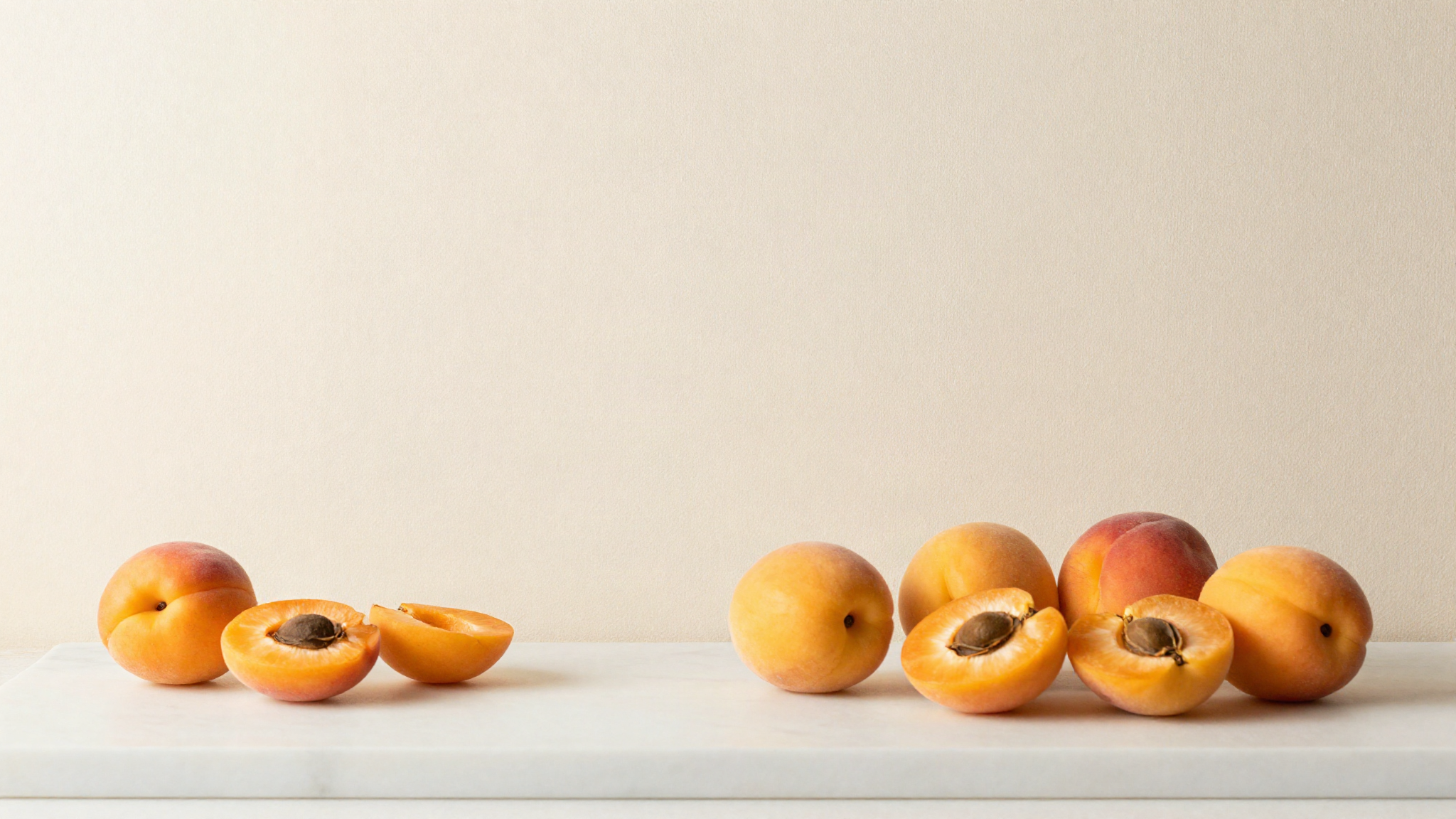 Ripe fresh apricots whole and halved showing their stones on white marble