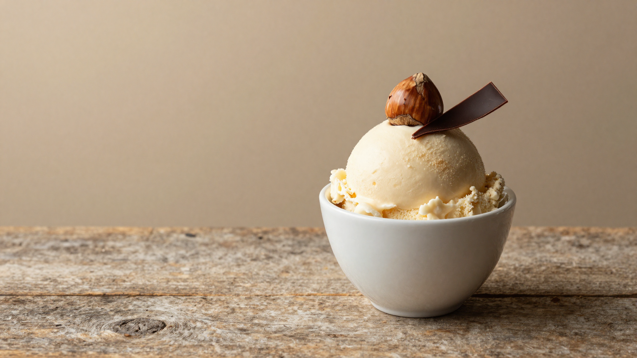 Finished bacio gelato scoop in white ceramic cup topped with a whole hazelnut and dark chocolate ribbon on aged wood