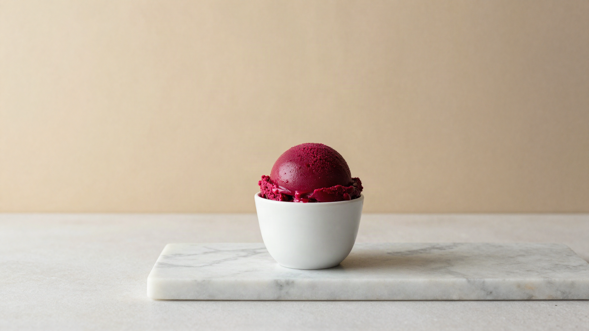A freshly drawn scoop of deep magenta beetroot sorbetto in a small white ceramic cup on marble