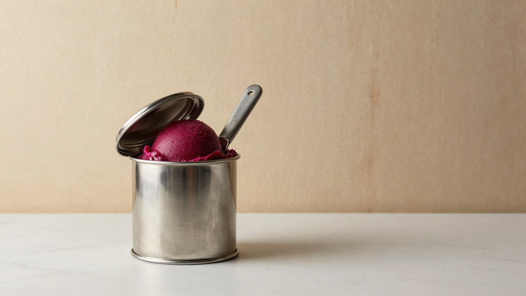 A covered stainless steel pozzetto well with a scoop of deep magenta prickly pear sorbetto inside, lid partly lifted