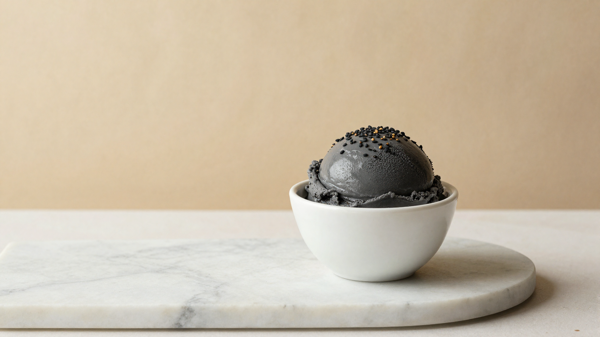 Dark slate-grey black sesame gelato in a white ceramic cup topped with toasted sesame seeds