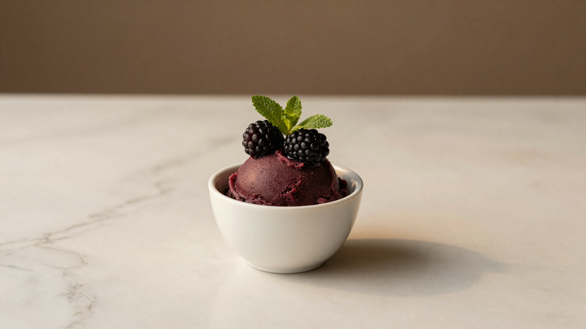 Dark blackberry sorbetto served in a white ceramic cup with fresh berries