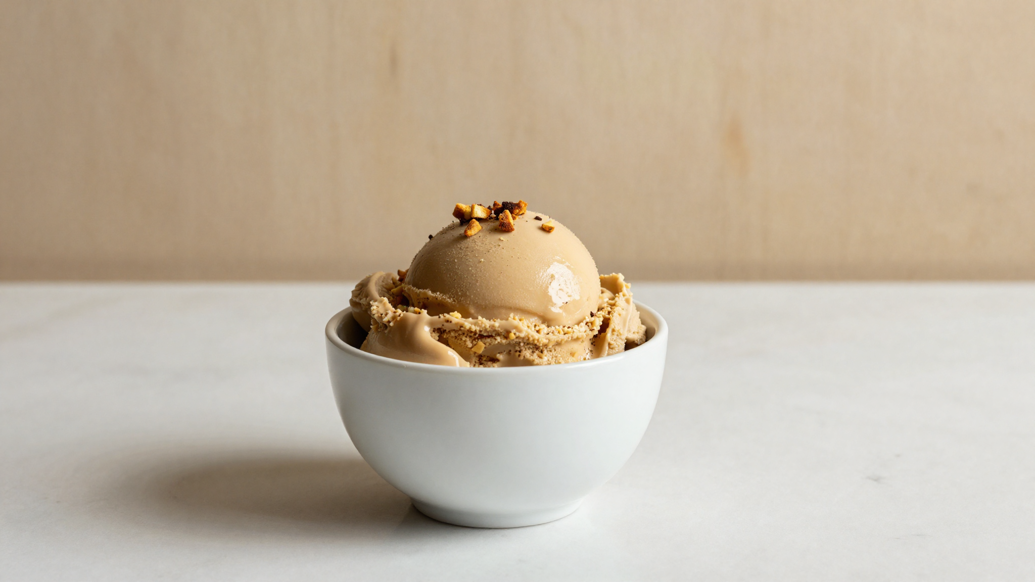 A serving of deep caramel brown butter gelato in a white ceramic cup on marble