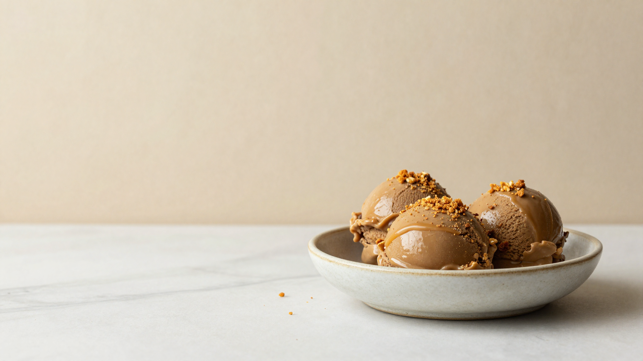 Three small scoops of deep caramel brown butter gelato in a shallow ceramic bowl