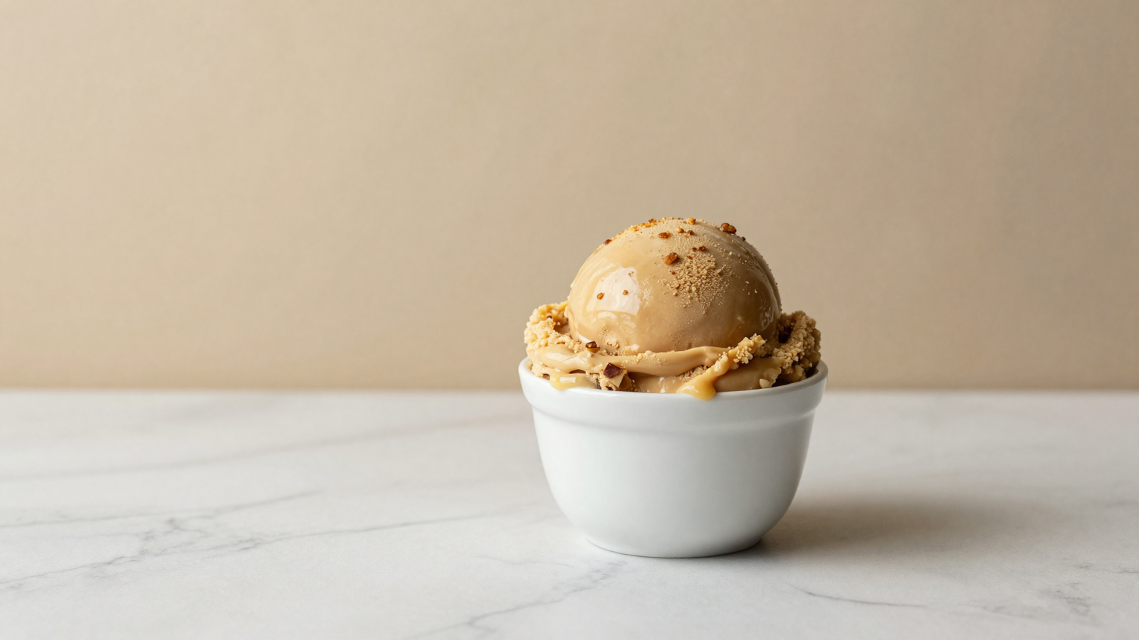 A glass bowl of pale gelato base beside a small dish of amber browned butter and a whisk on a marble lab counter