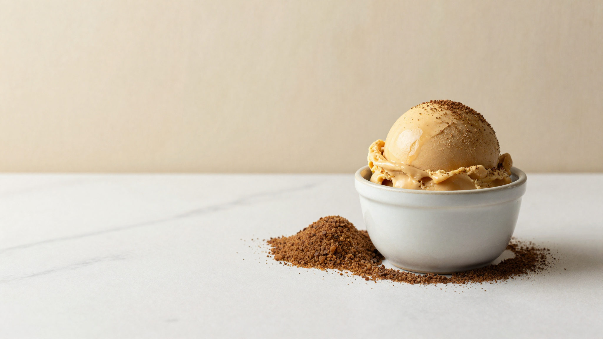 A mound of dark muscovado brown sugar beside a scoop of caramel-toned gelato in a ceramic cup on marble