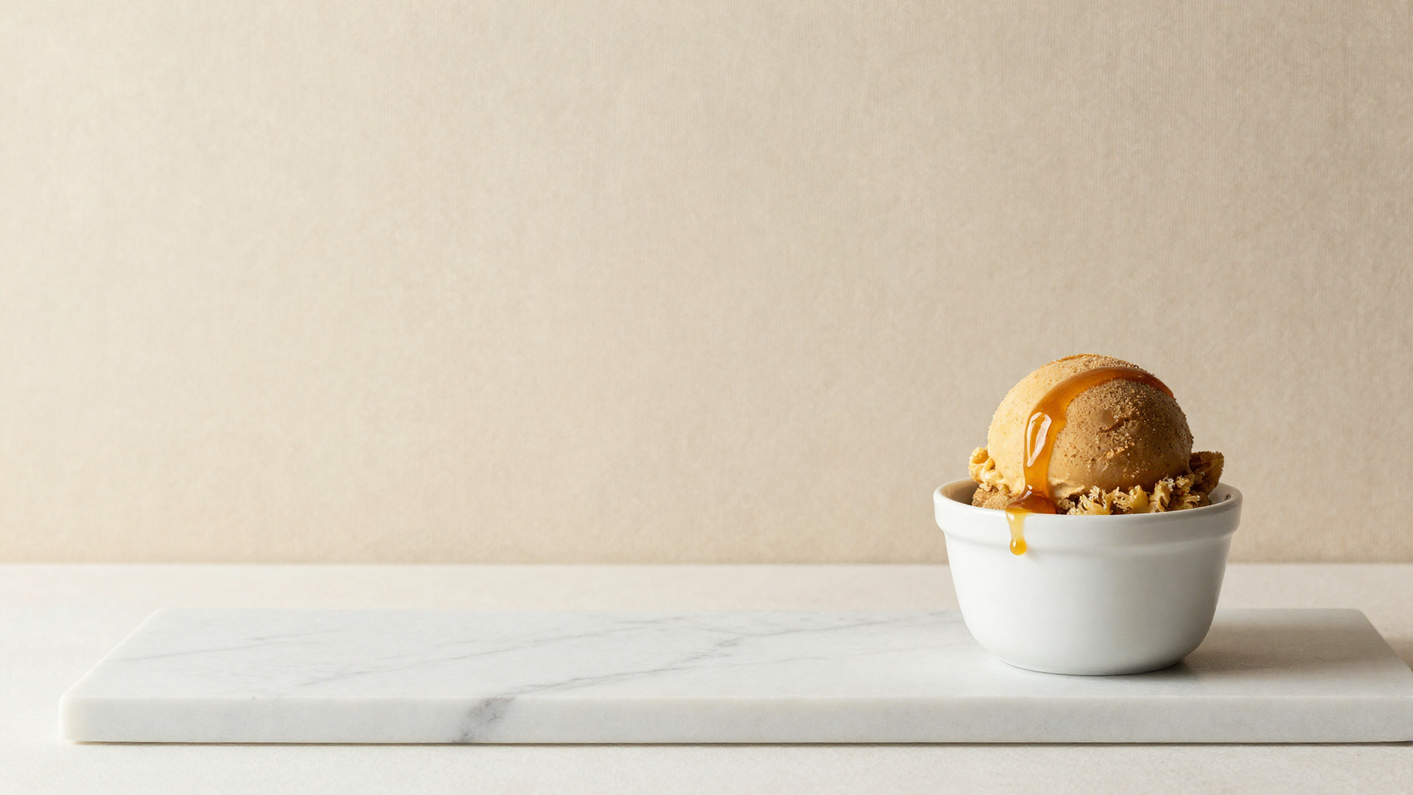 A scoop of amber brown-sugar gelato in a white ceramic cup lightly drizzled with caramel on marble
