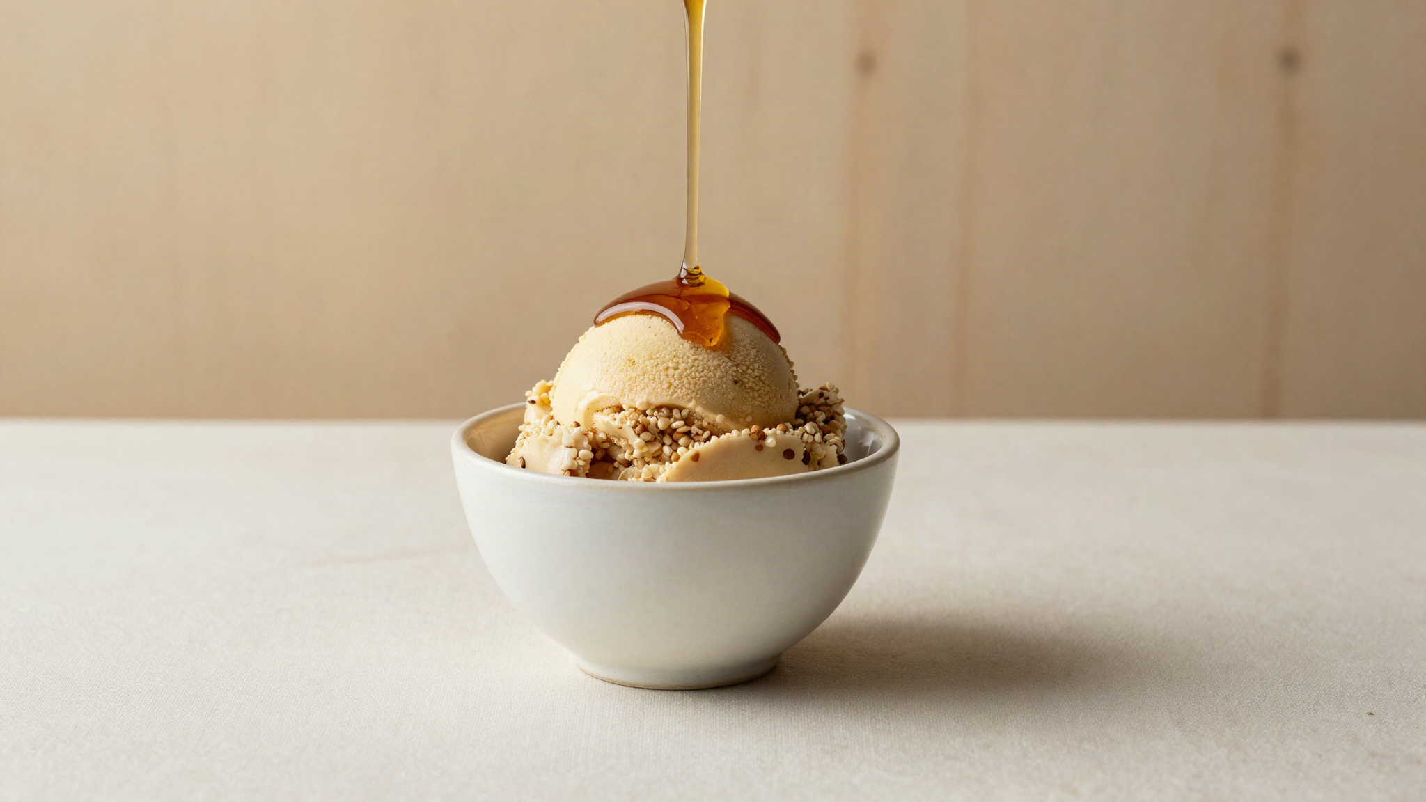 A serving of tan buckwheat honey gelato in a ceramic cup with a thin drizzle of dark honey