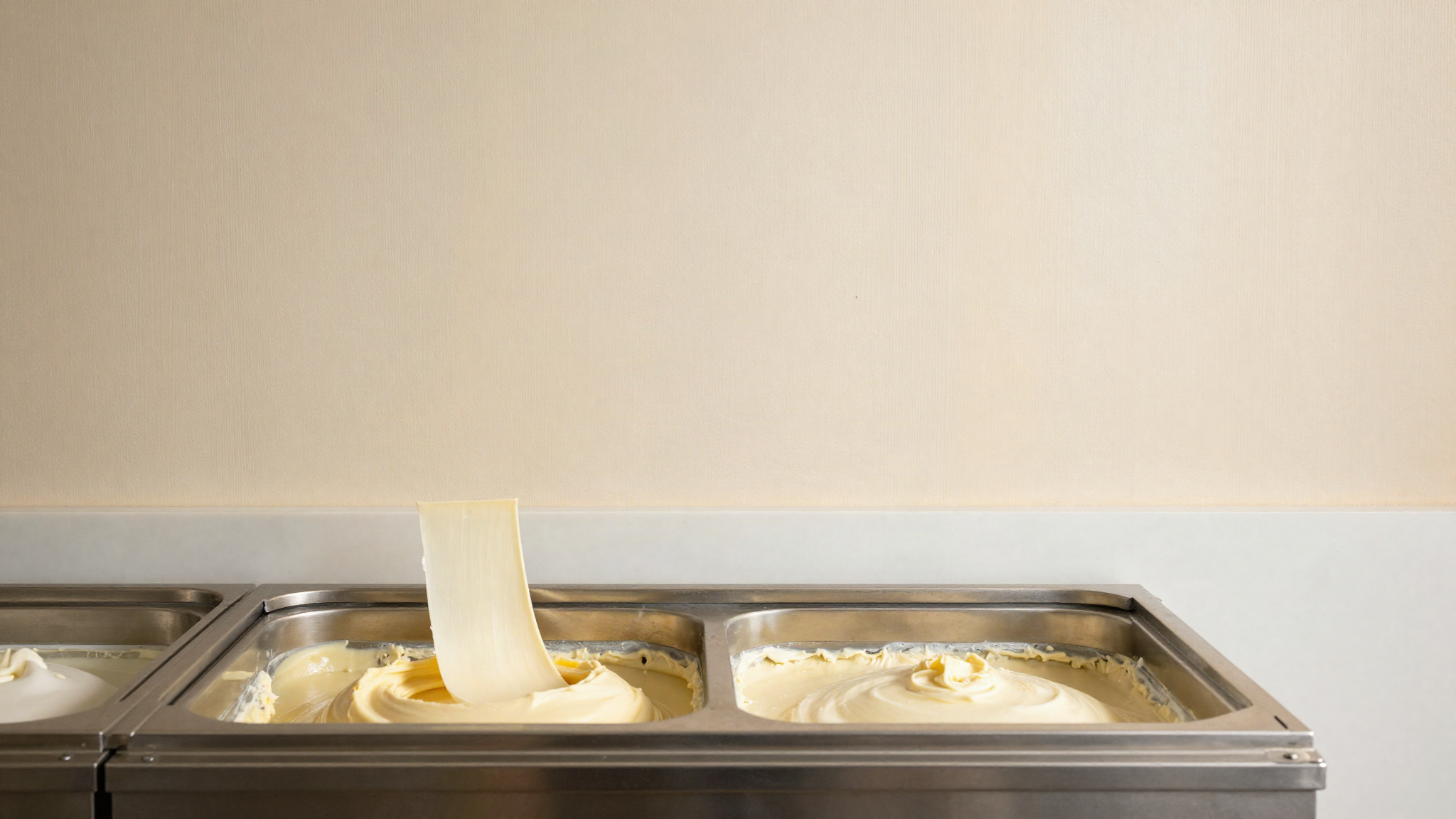 A batch freezer dasher lifting thick pale gelato ribbons in a gelato lab