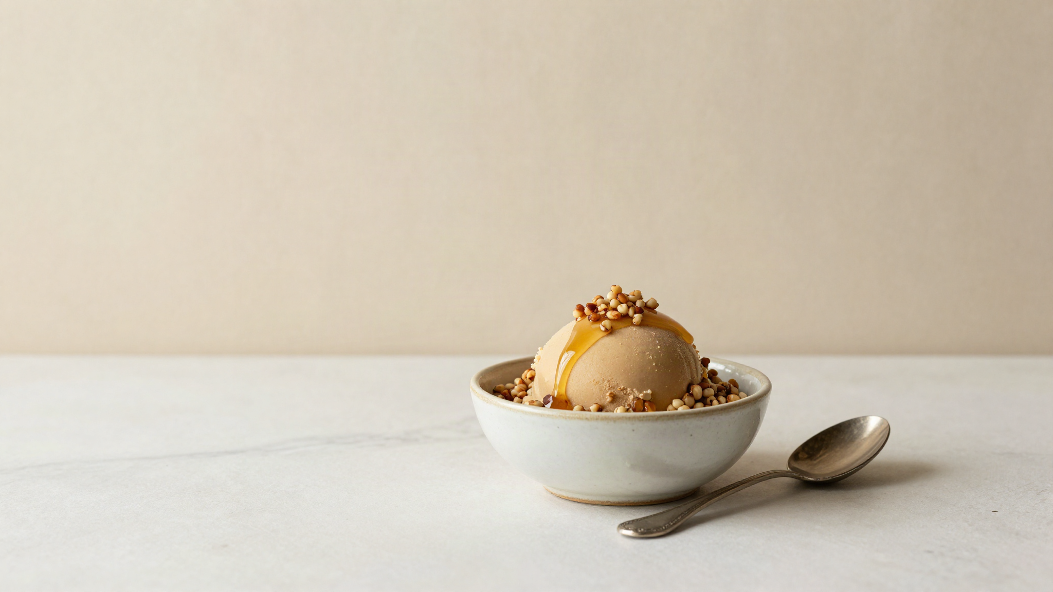 A ceramic bowl of buckwheat honey gelato topped with toasted groats and a honey drizzle
