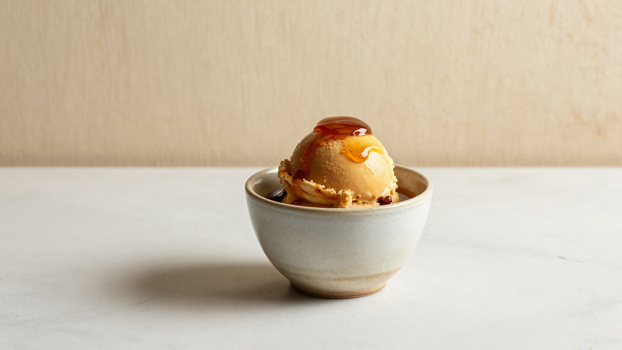 A cup of deep amber burnt honey gelato with a thin honey drizzle on marble