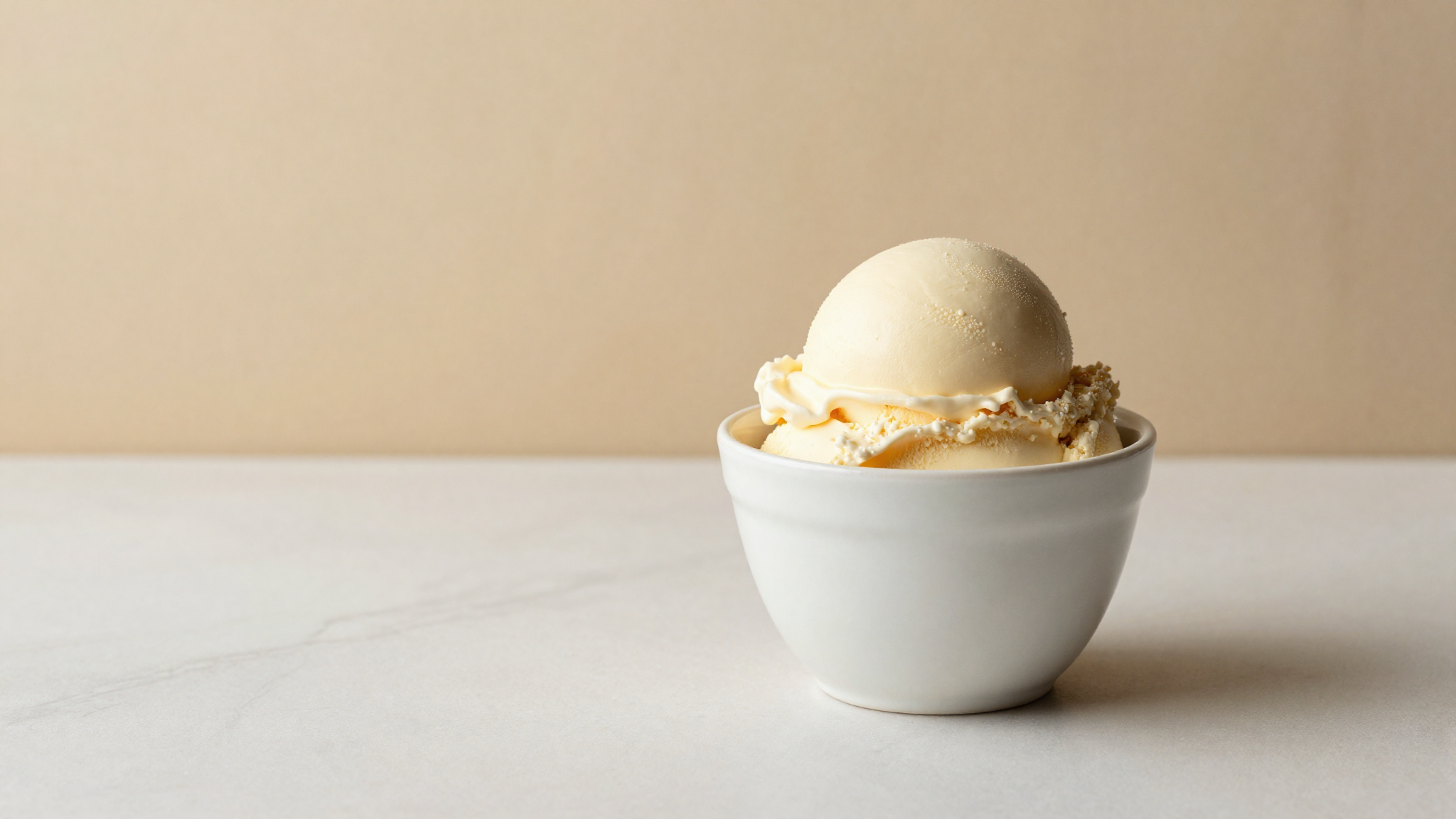 A white ceramic cup of pale ivory buttermilk gelato, simply garnished, on a pale counter