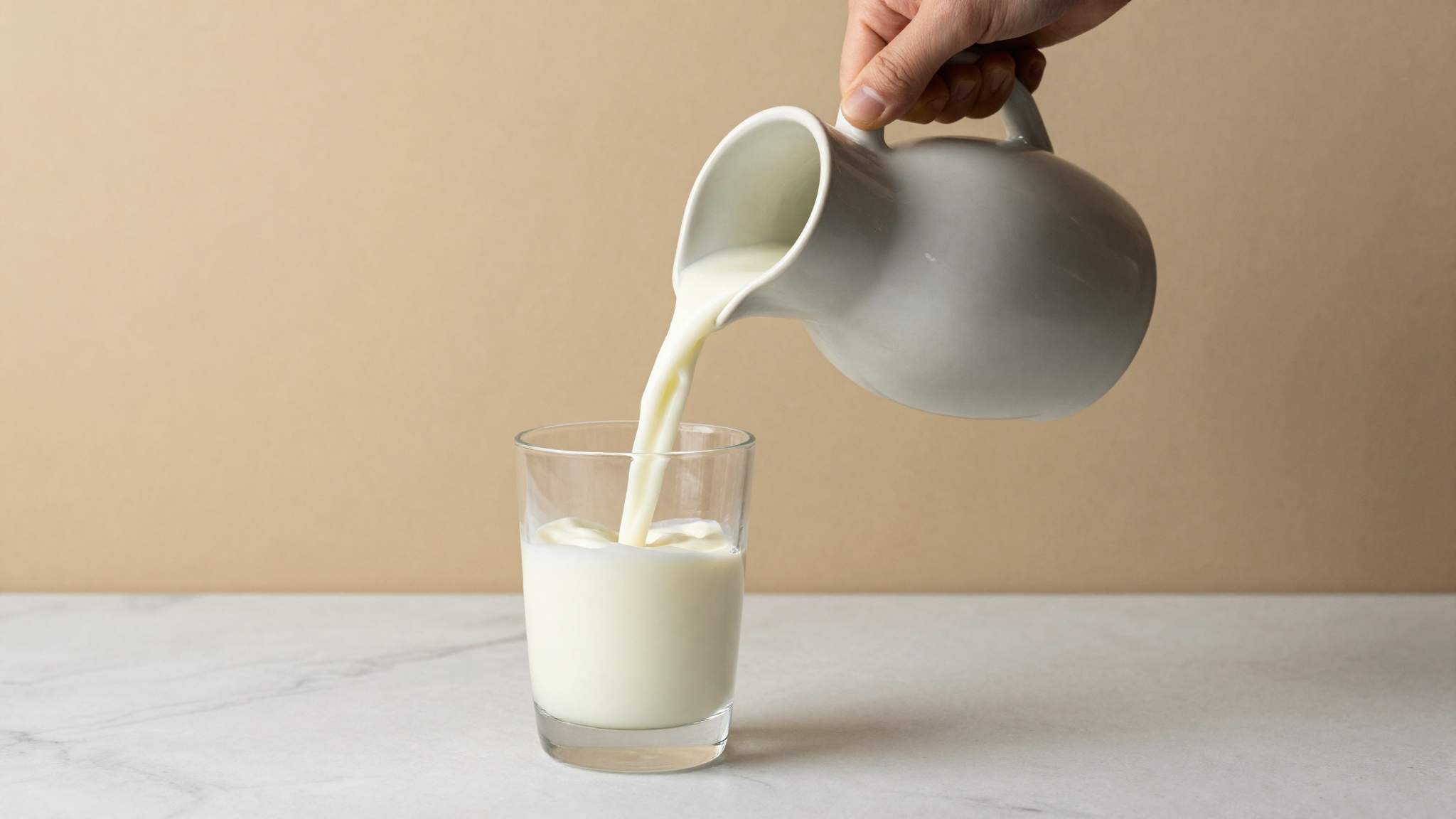 Cultured buttermilk being poured from a ceramic jug into a glass on a marble counter