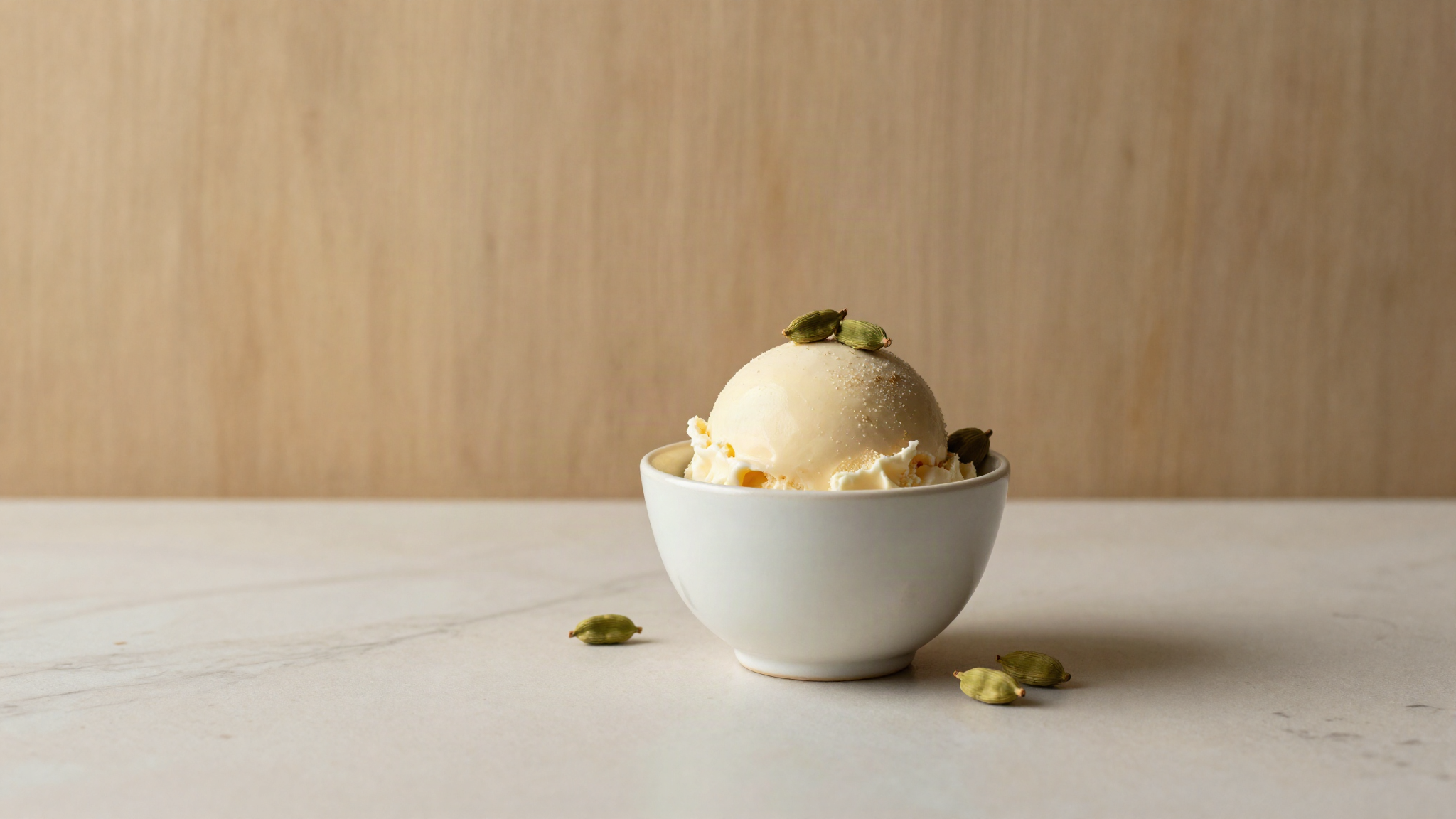 Cardamom gelato in a refined ceramic cup with green cardamom pods beside it on marble