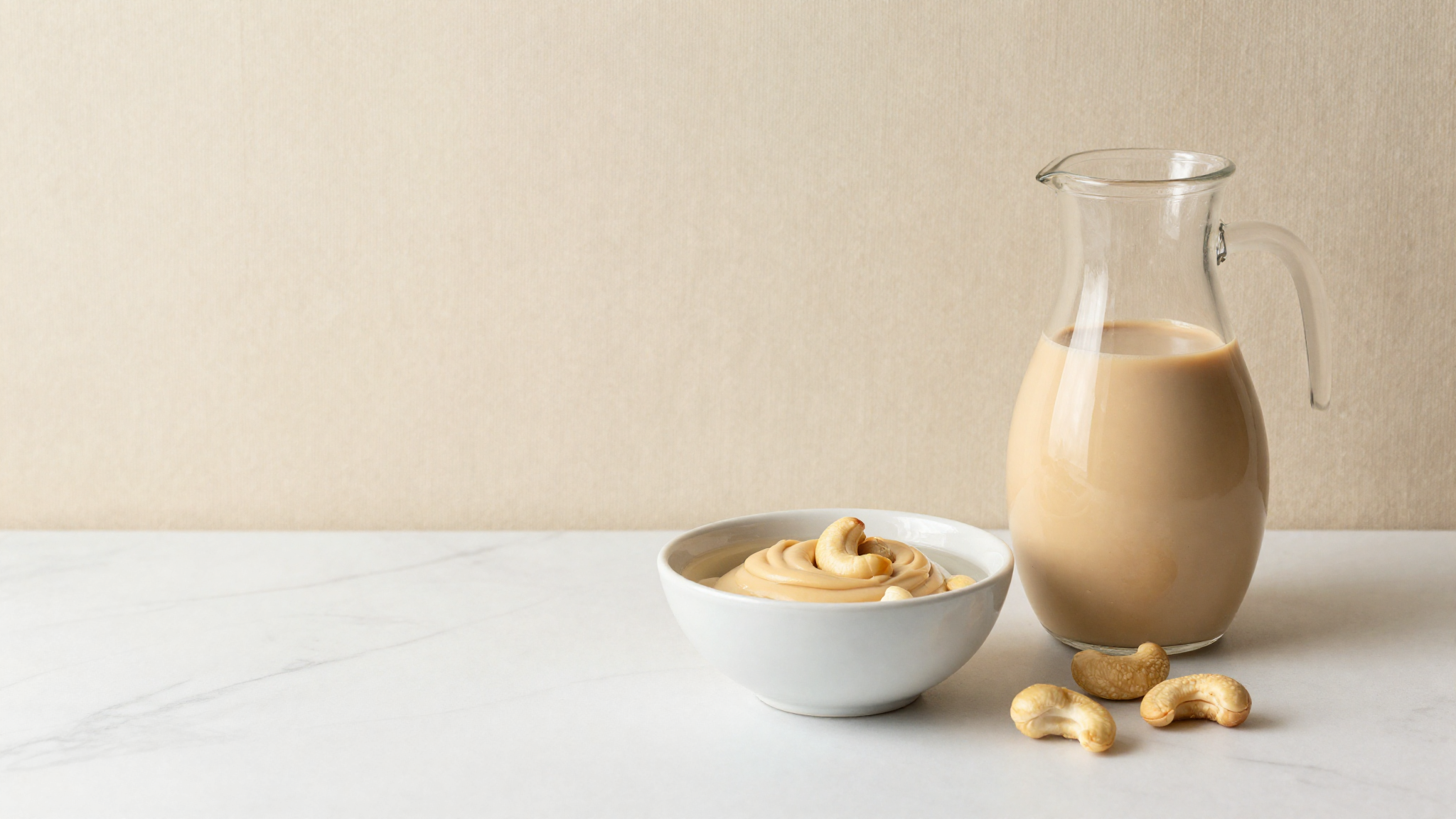 Raw cashews soaking beside a jug of smooth blended cashew cream on marble