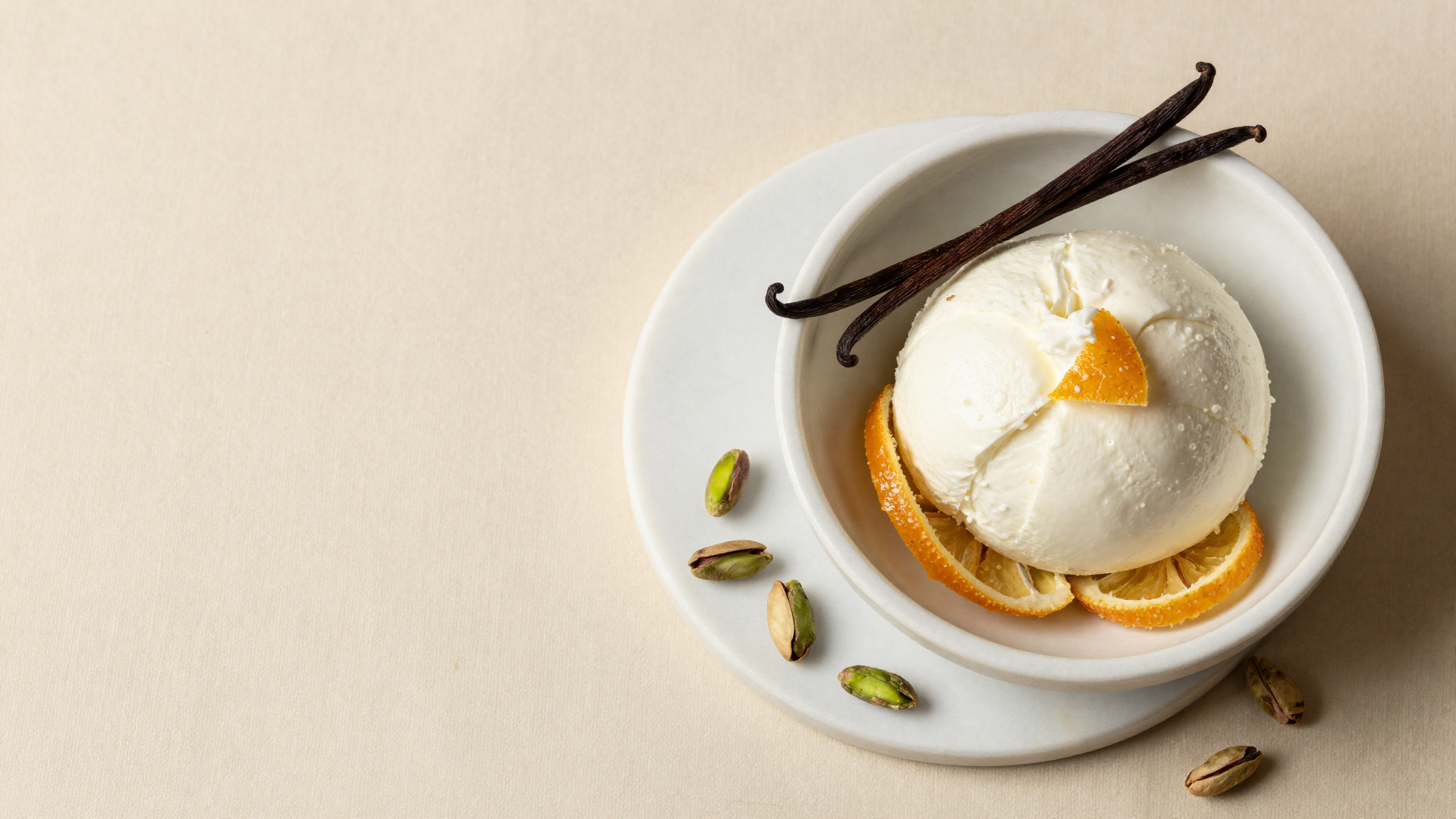 Top down still life on white marble of fresh sheep ricotta in a ceramic bowl, candied citrus peel, shelled pistachios and a vanilla pod