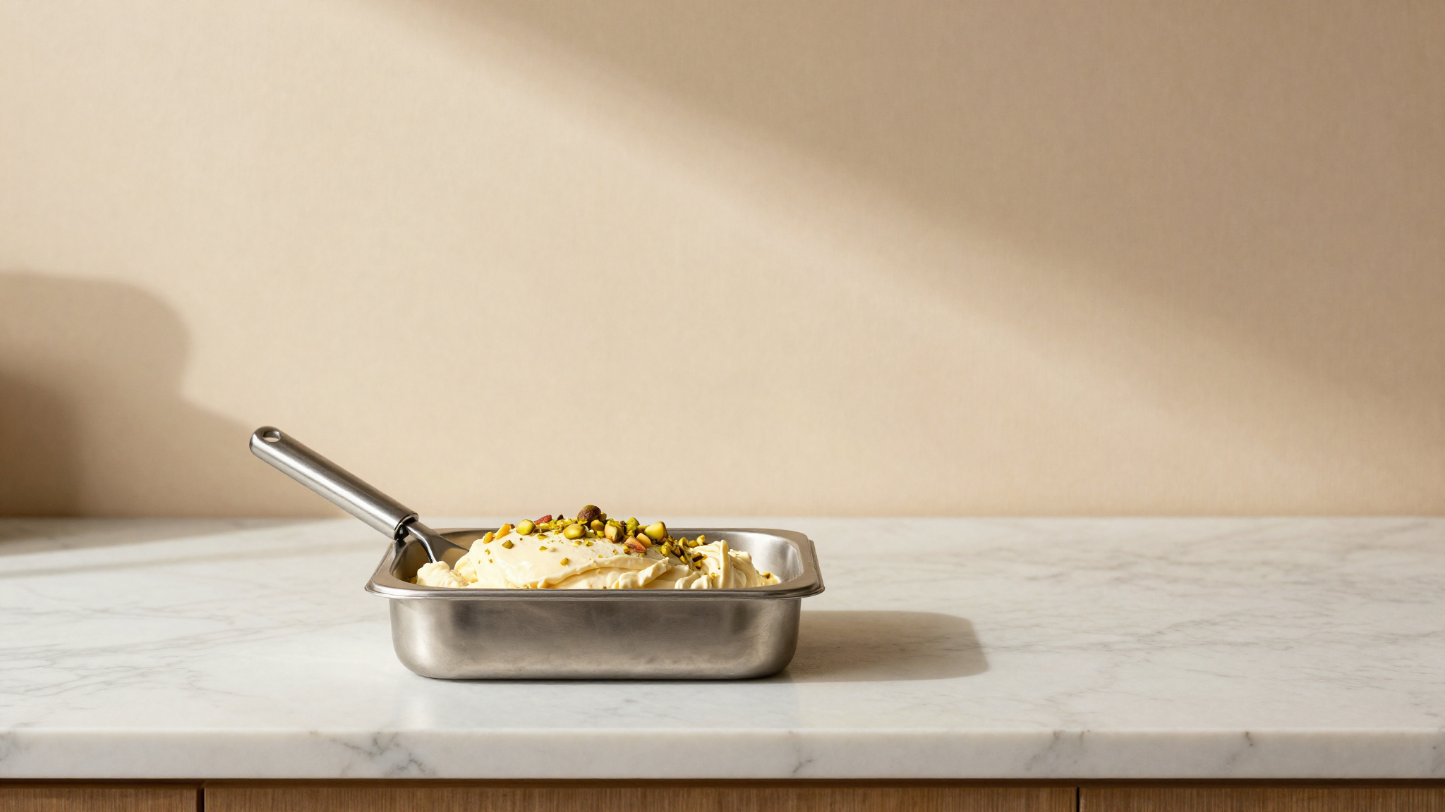 Stainless steel gelato pan freshly drawn from a mantecatore showing creamy cassata mix with flecks of candied fruit and pistachio