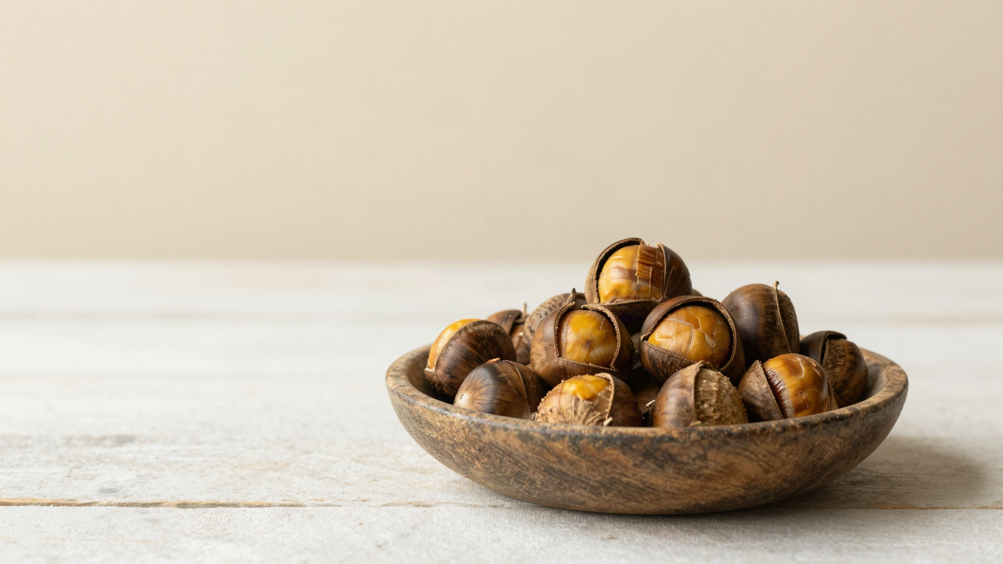 Roasted chestnuts split open in a rustic shallow bowl on aged wood