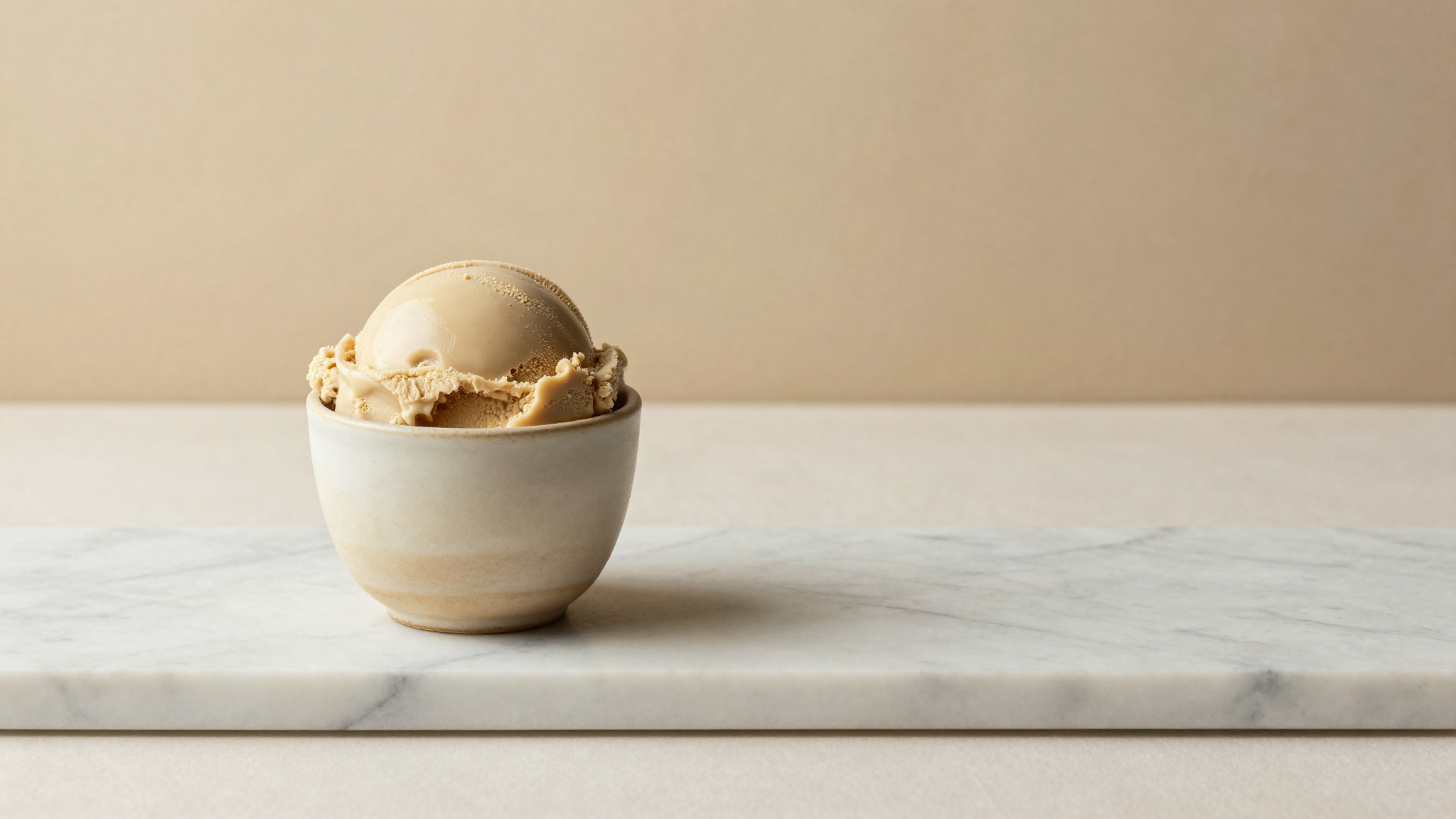 A small ceramic cup of pale beige chestnut gelato on marble, smooth dense surface