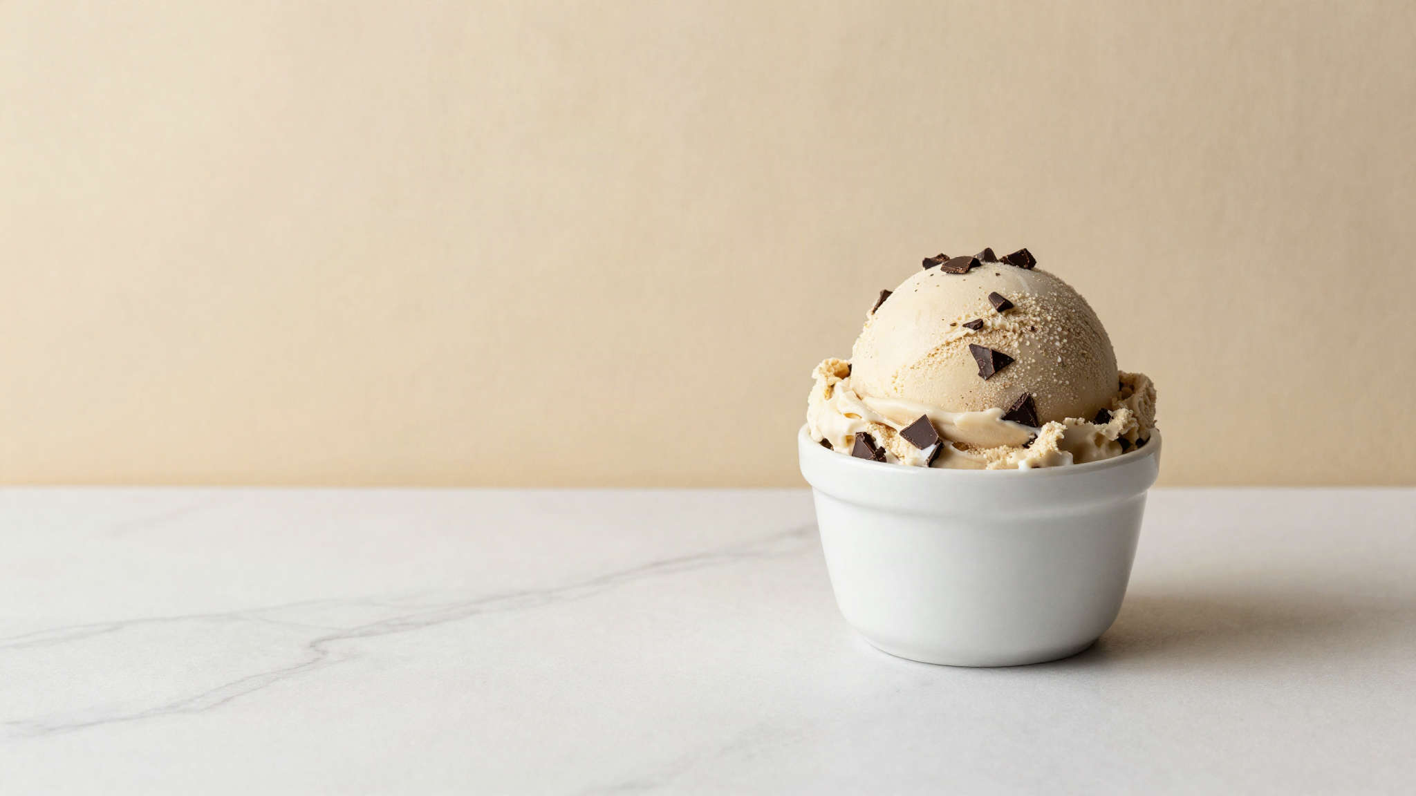 A scoop of italian chocolate chip gelato in a white ceramic cup on marble with dark chocolate shards visible