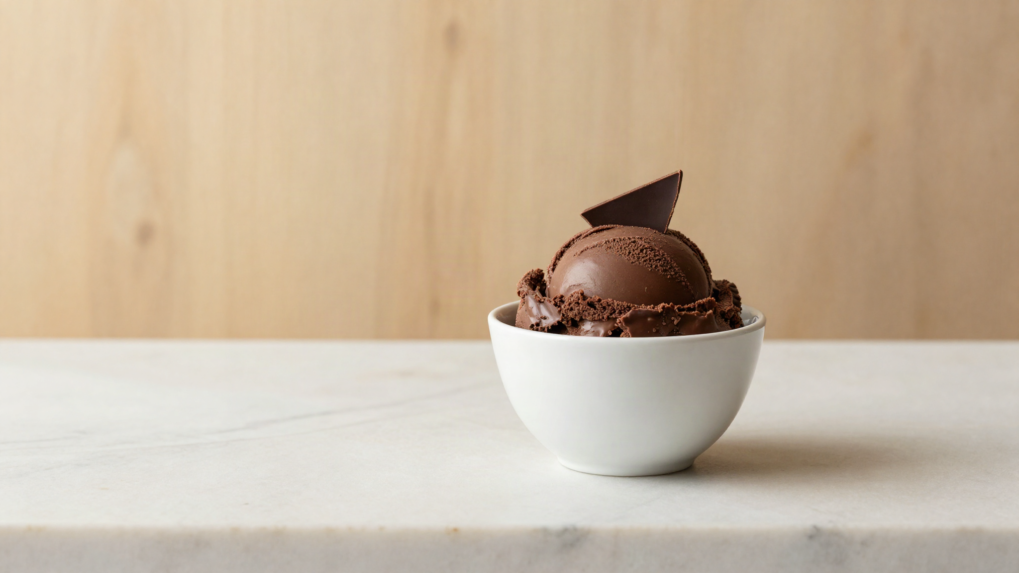 Intense dark chocolate gelato in a white ceramic cup with a chocolate shard on marble