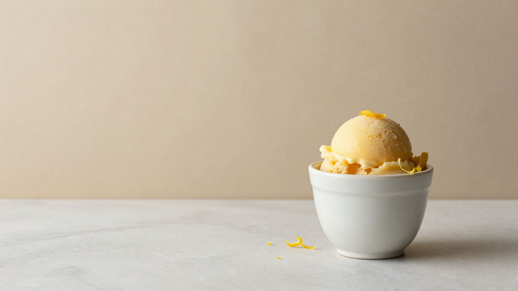Scoop of smooth citrus sorbet in a chilled ceramic cup on marble with a curl of lemon zest