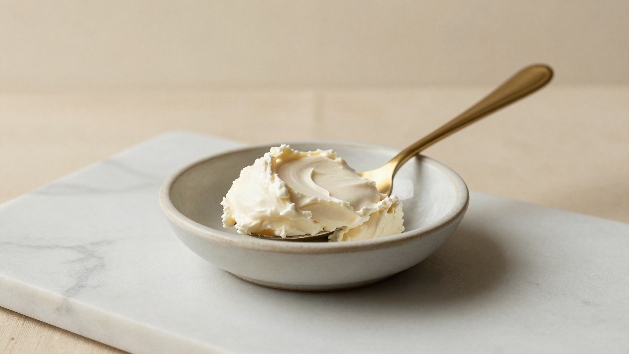 A thick spoonful of golden crusted clotted cream in a small ceramic dish on marble
