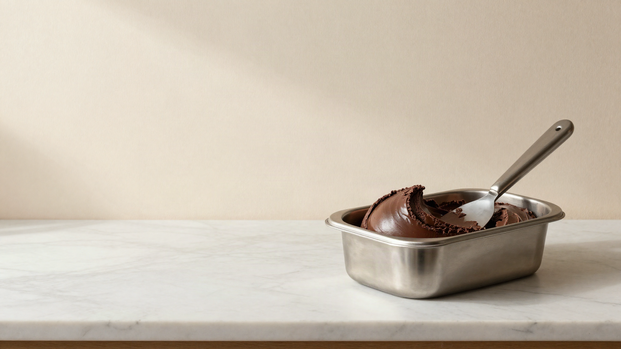 Stainless gelato pan of glossy dark chocolate gelato with a spatula resting across it