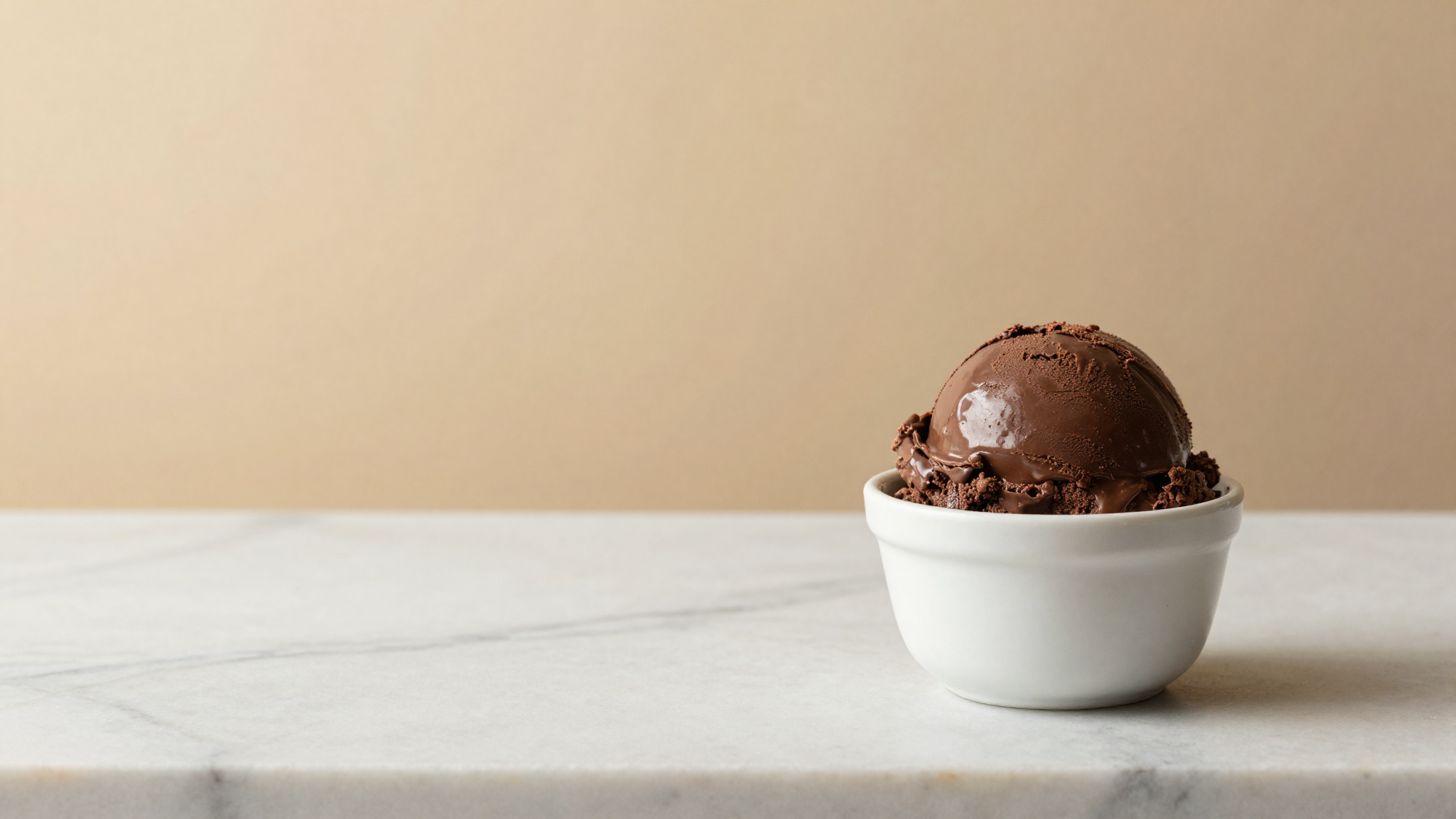 Glossy dark chocolate gelato scoop in a white ceramic cup on marble counter