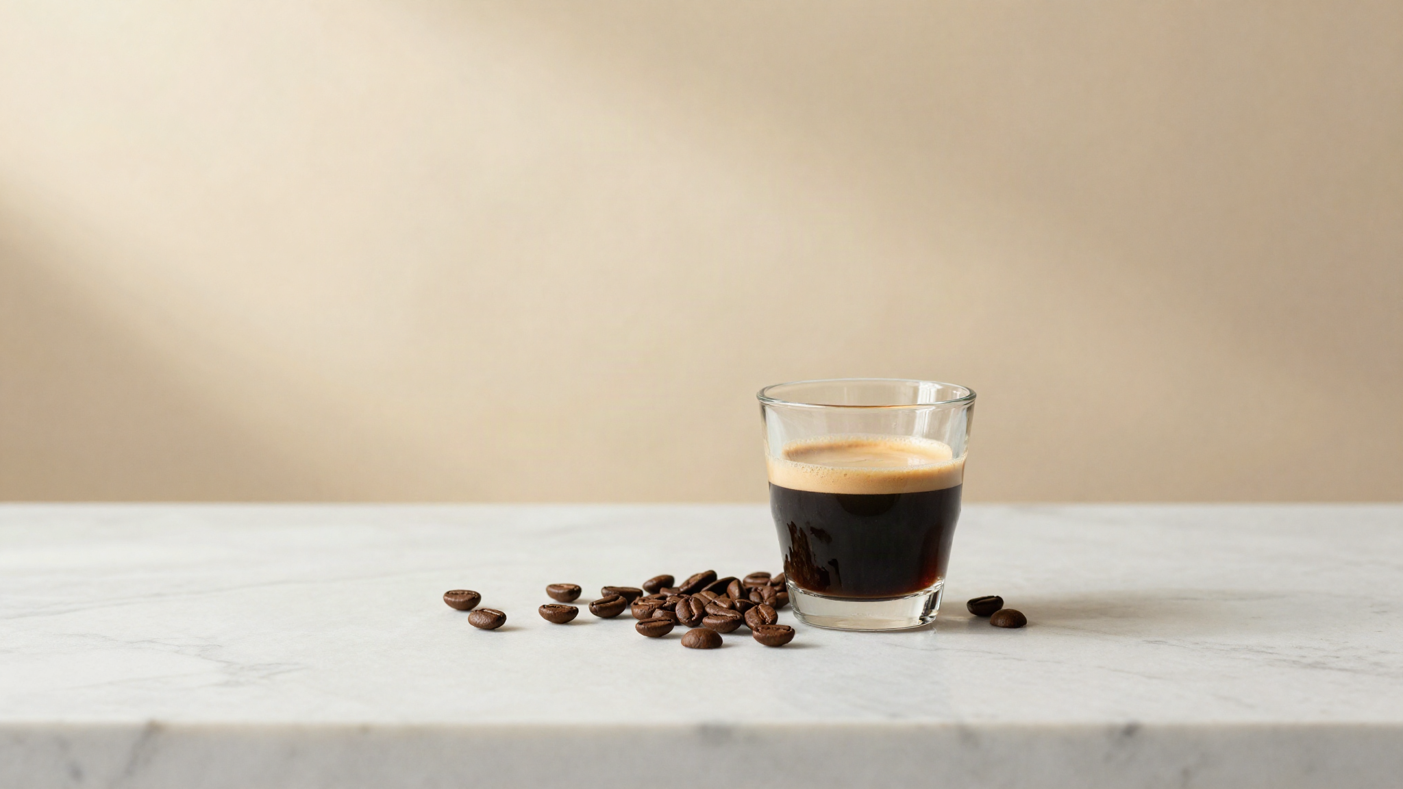 Glass of freshly pulled espresso beside whole roasted coffee beans on marble