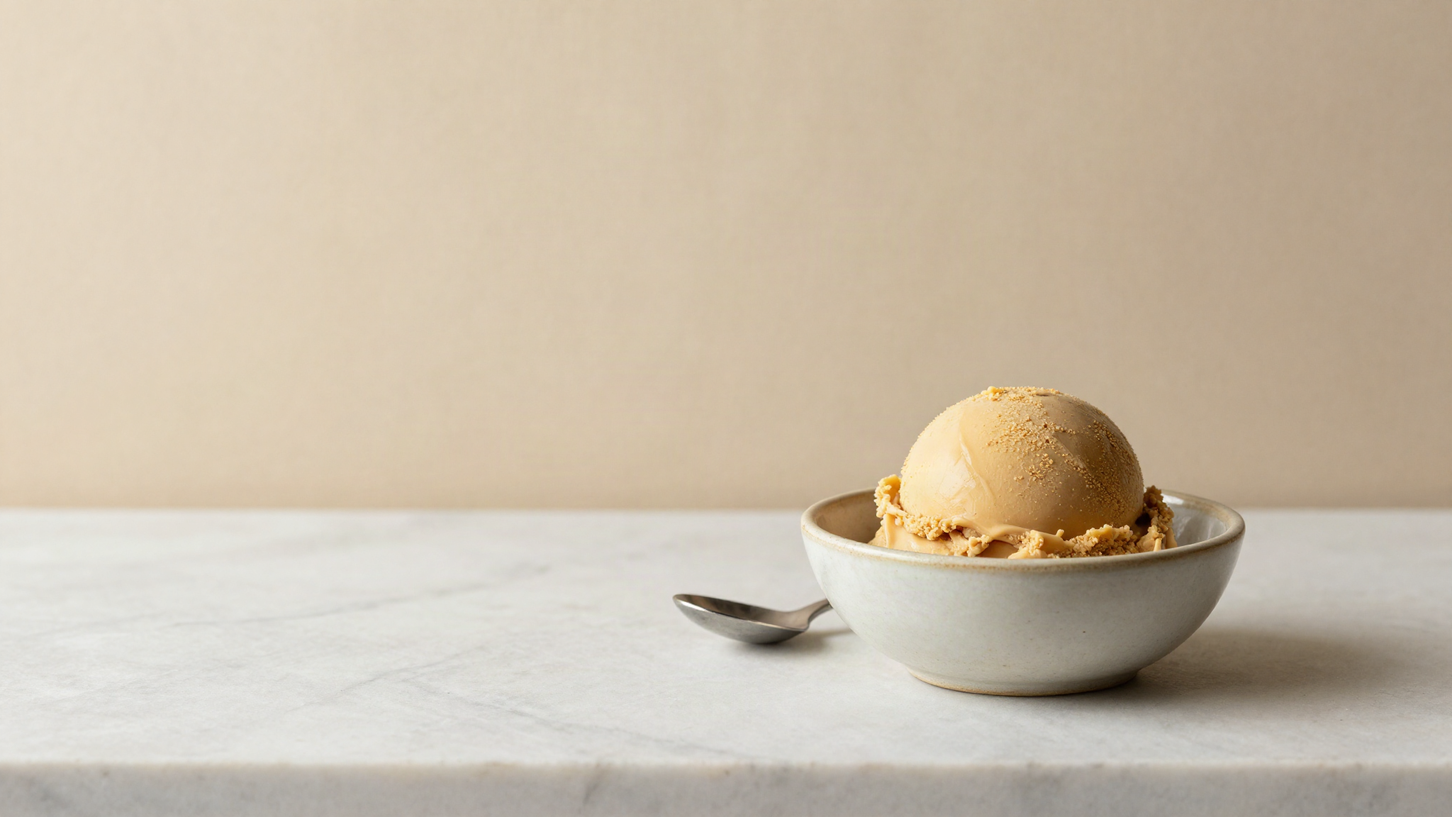 Single scoop of coffee gelato in a chilled ceramic bowl with a small spoon on marble