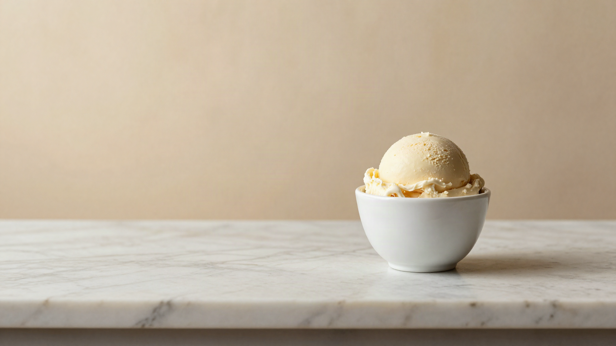 A dense glossy scoop of pale sicilian style gelato in a small white ceramic cup on marble