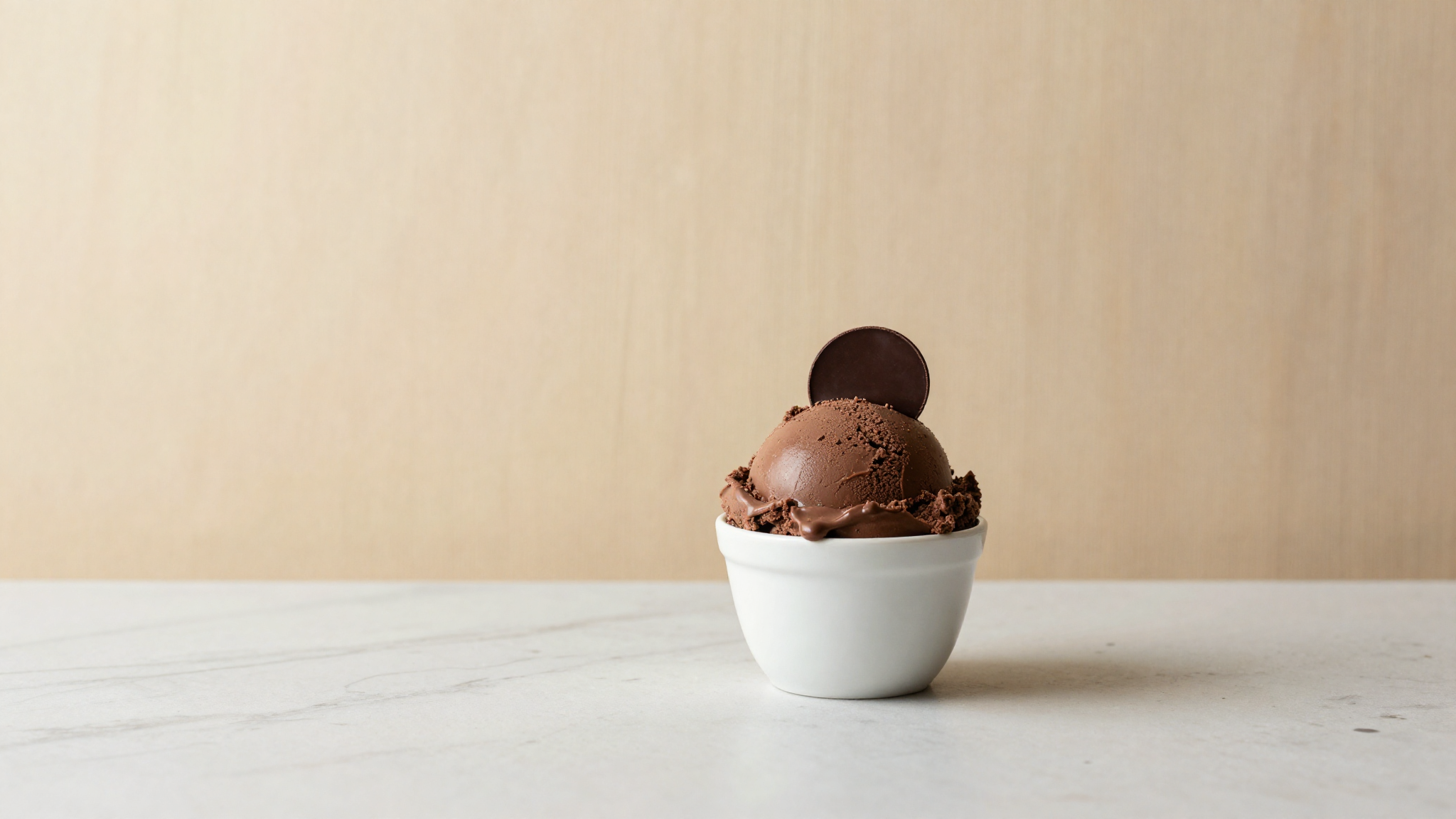 A scoop of rich dark chocolate gelato in a white ceramic cup with a single couverture disc as garnish