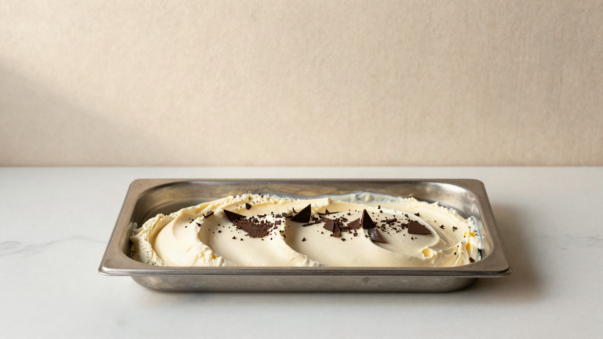 A stainless steel pan of stracciatella with thin dark chocolate shards folded through the surface