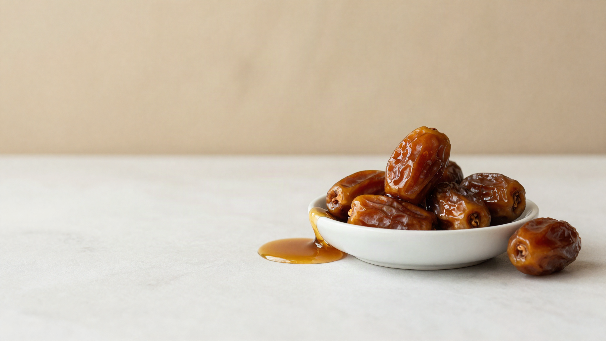 Dark glossy date syrup pooling in a white ceramic dish beside whole medjool dates on marble