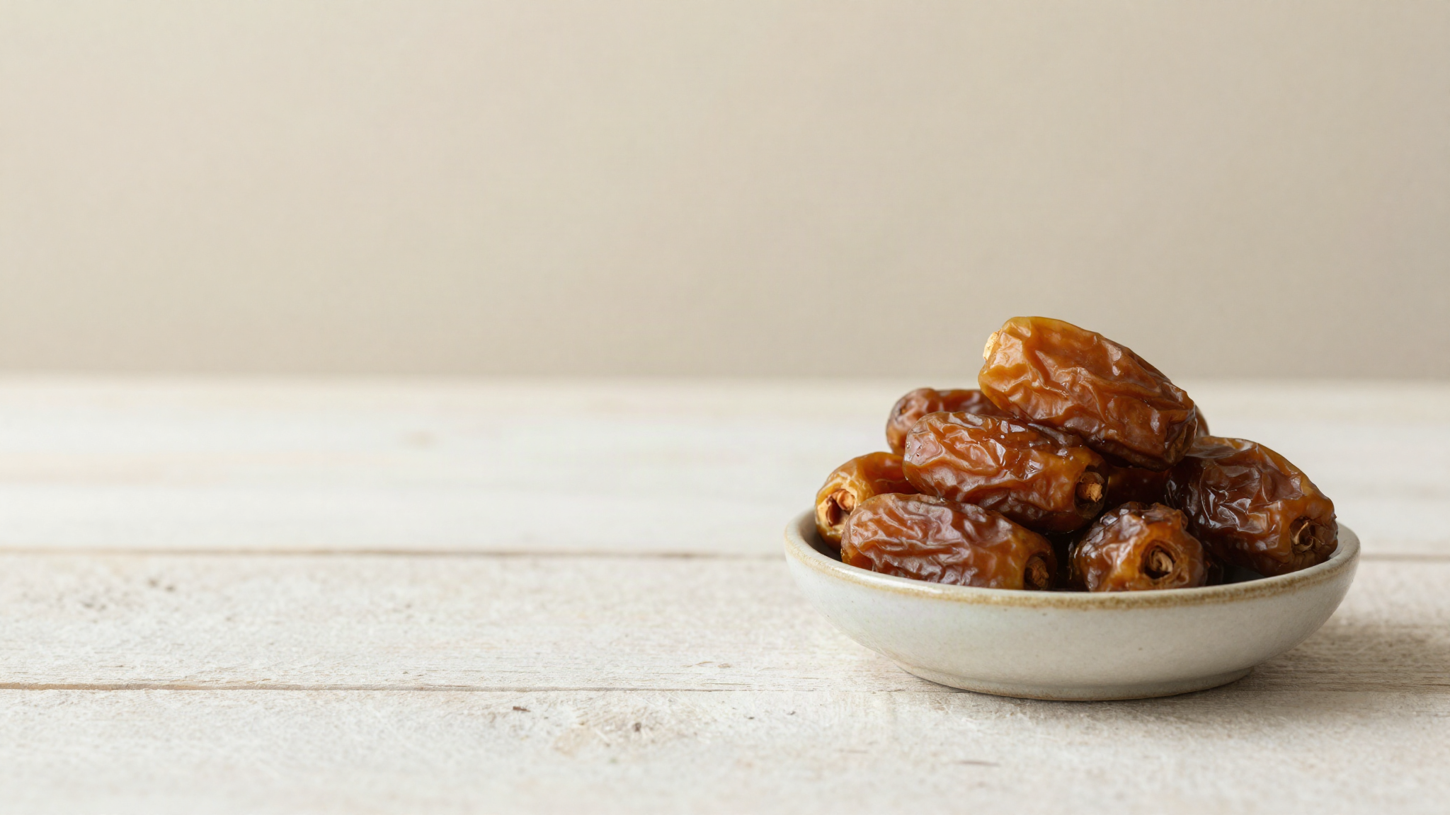 Whole medjool dates in a small ceramic bowl on aged wood, one split open showing the flesh