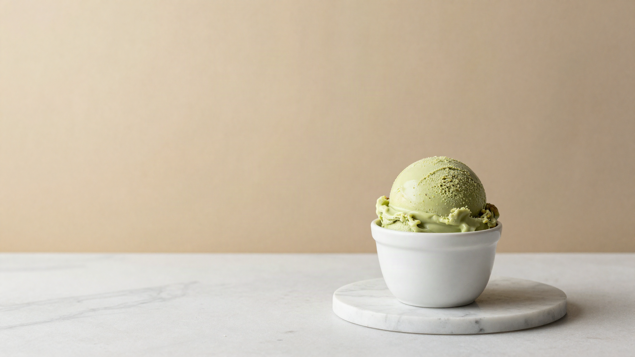 A freshly drawn scoop of pale green pistachio gelato in a small white ceramic cup on marble