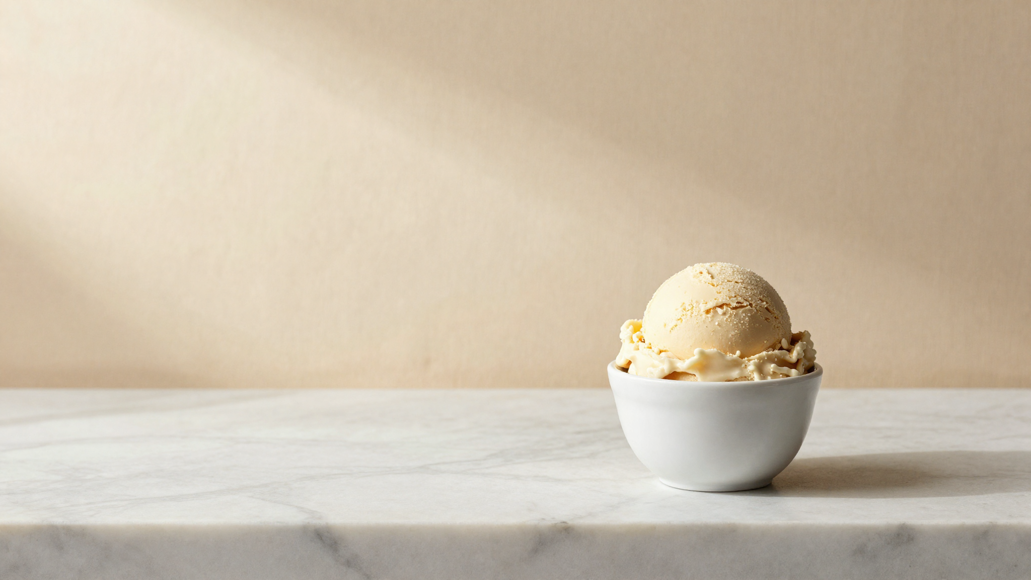 A scoop of Italian gelato in a small white ceramic cup on marble, conceptual still life