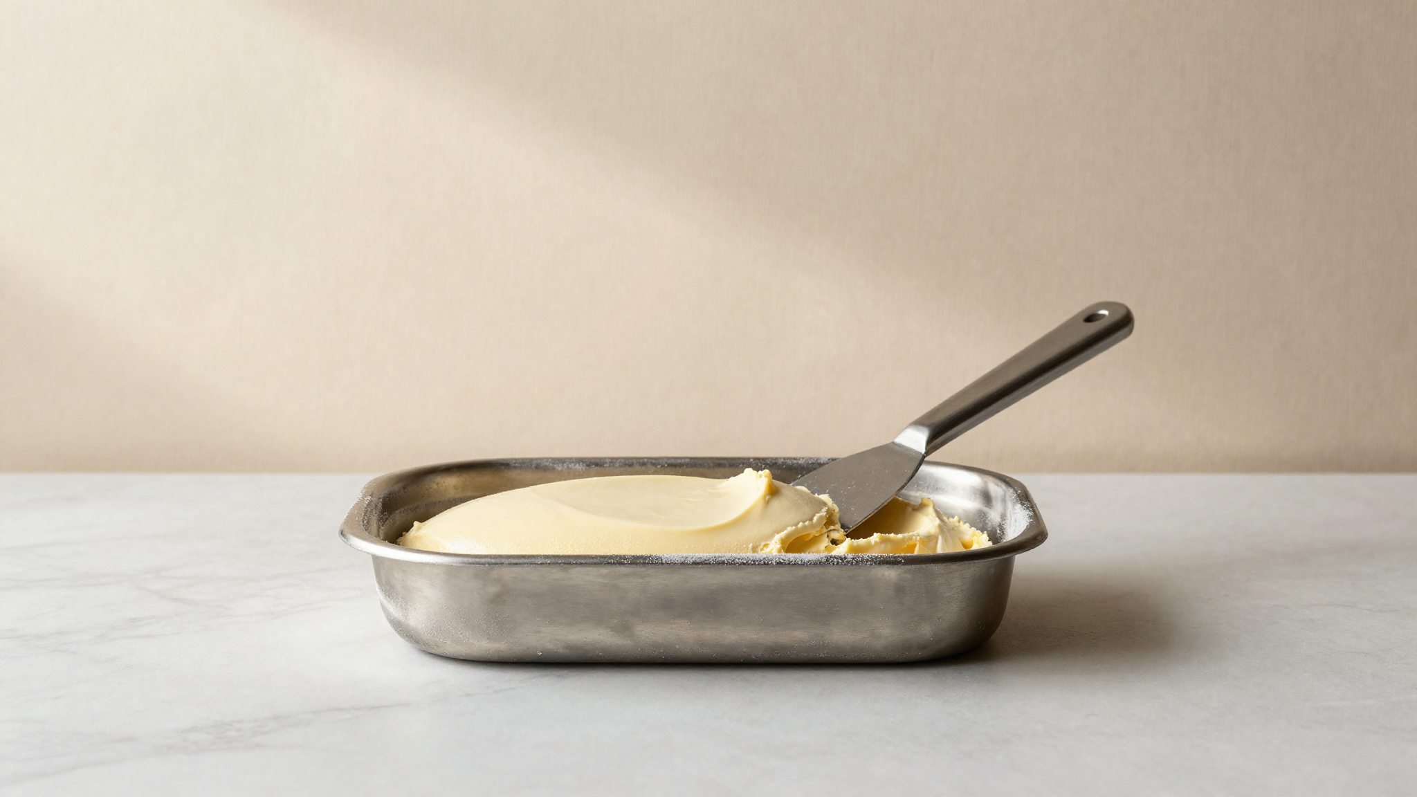 A stainless pan of freshly drawn gelato being leveled flat with a spatula before blast freezing