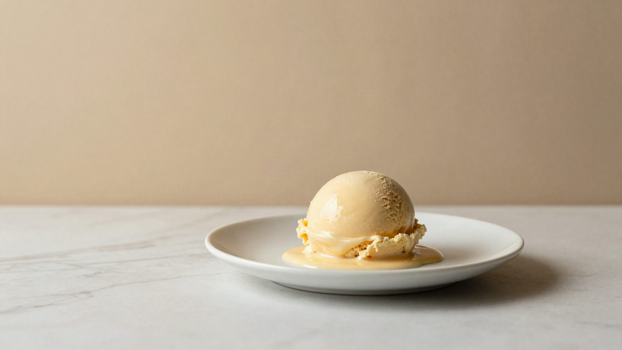A single scoop of gelato slowly slumping and glossing over on a white ceramic plate at room temperature