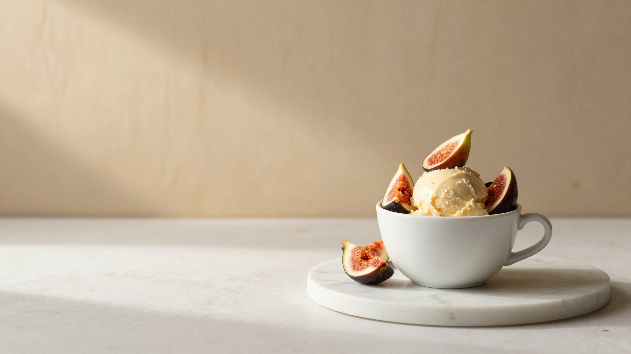 Finished fig gelato in a refined white ceramic cup garnished with fresh halved figs on white marble