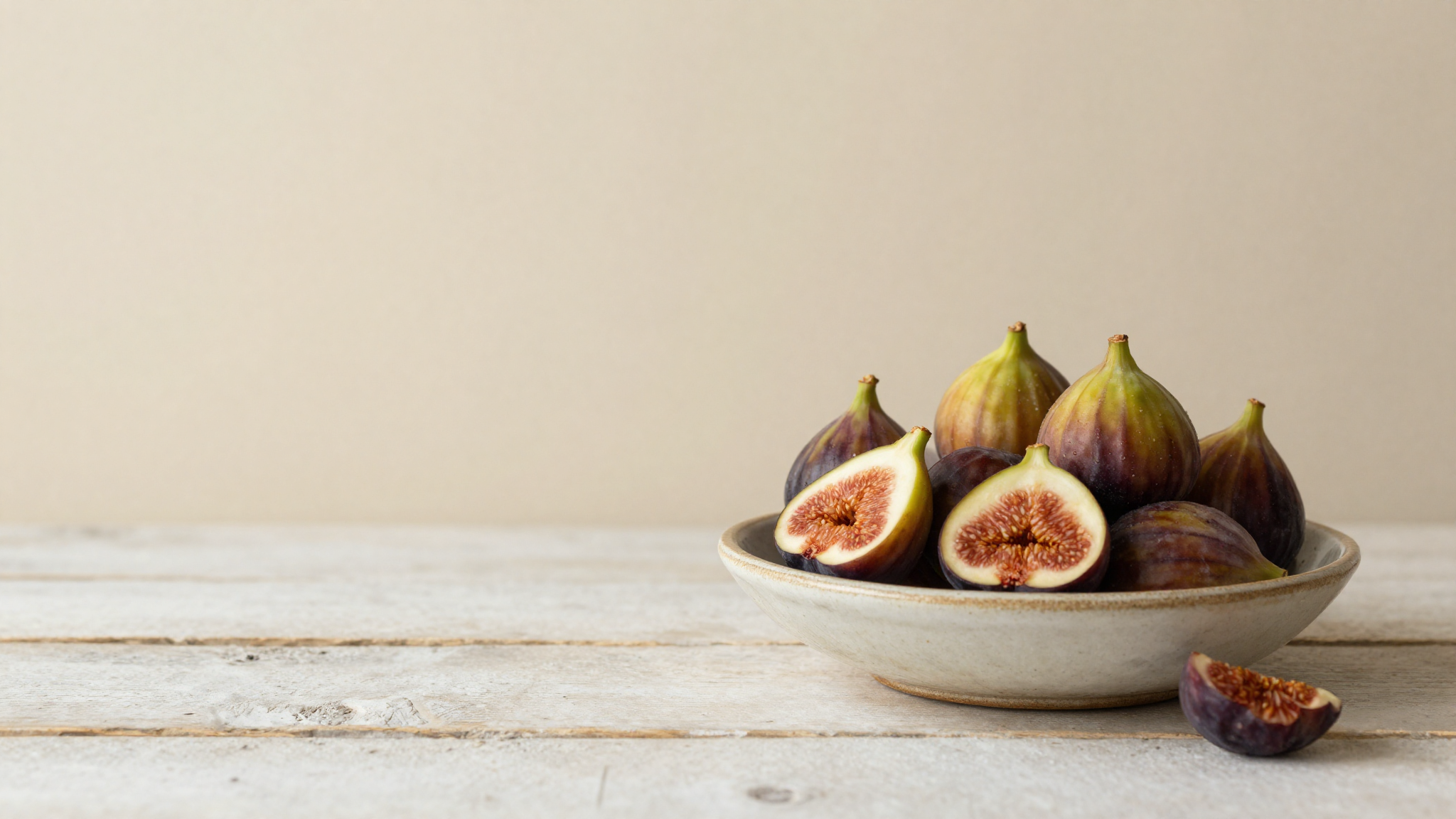 Ripe fresh figs whole and halved in a rustic ceramic bowl on aged wood, late summer harvest mood